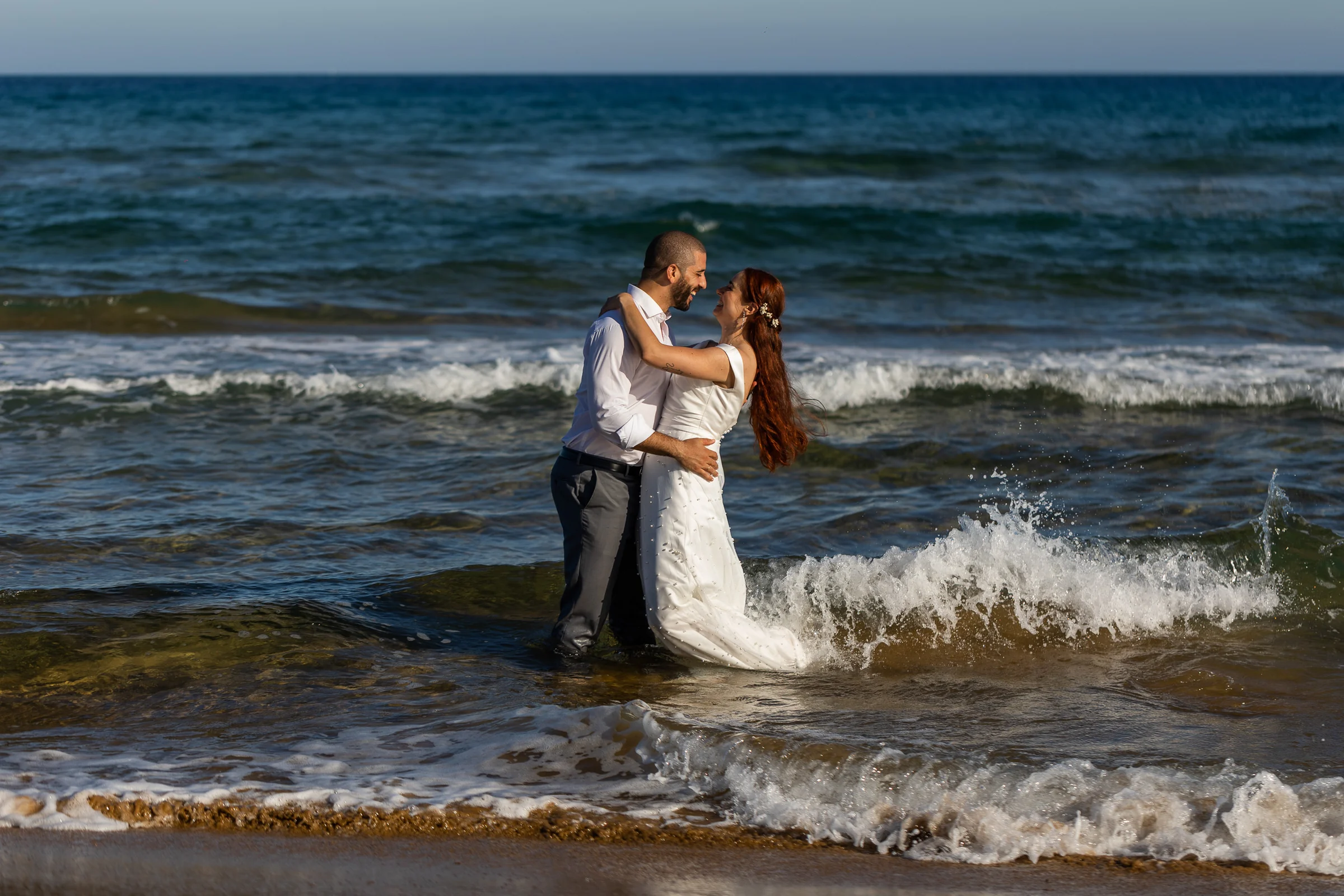 Noemí y Fran se abrazan dentro del mar mientras una ola salpica junto a ellos durante su postboda en Cartagena.
