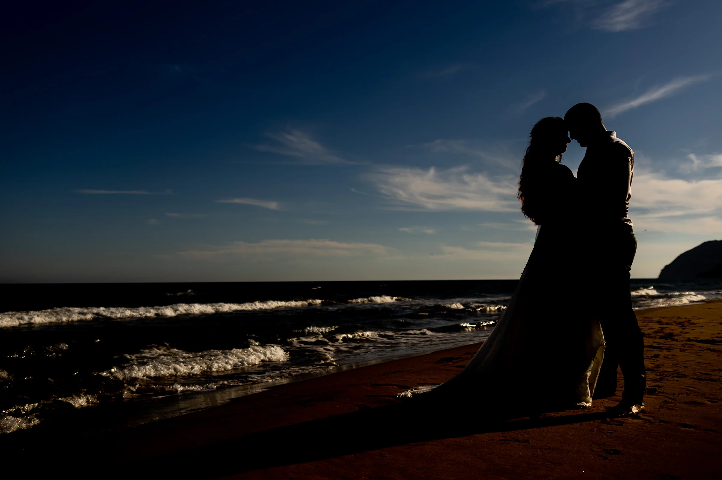 Silueta de Noemí y Fran abrazados al atardecer en la playa durante su postboda en Cartagena.