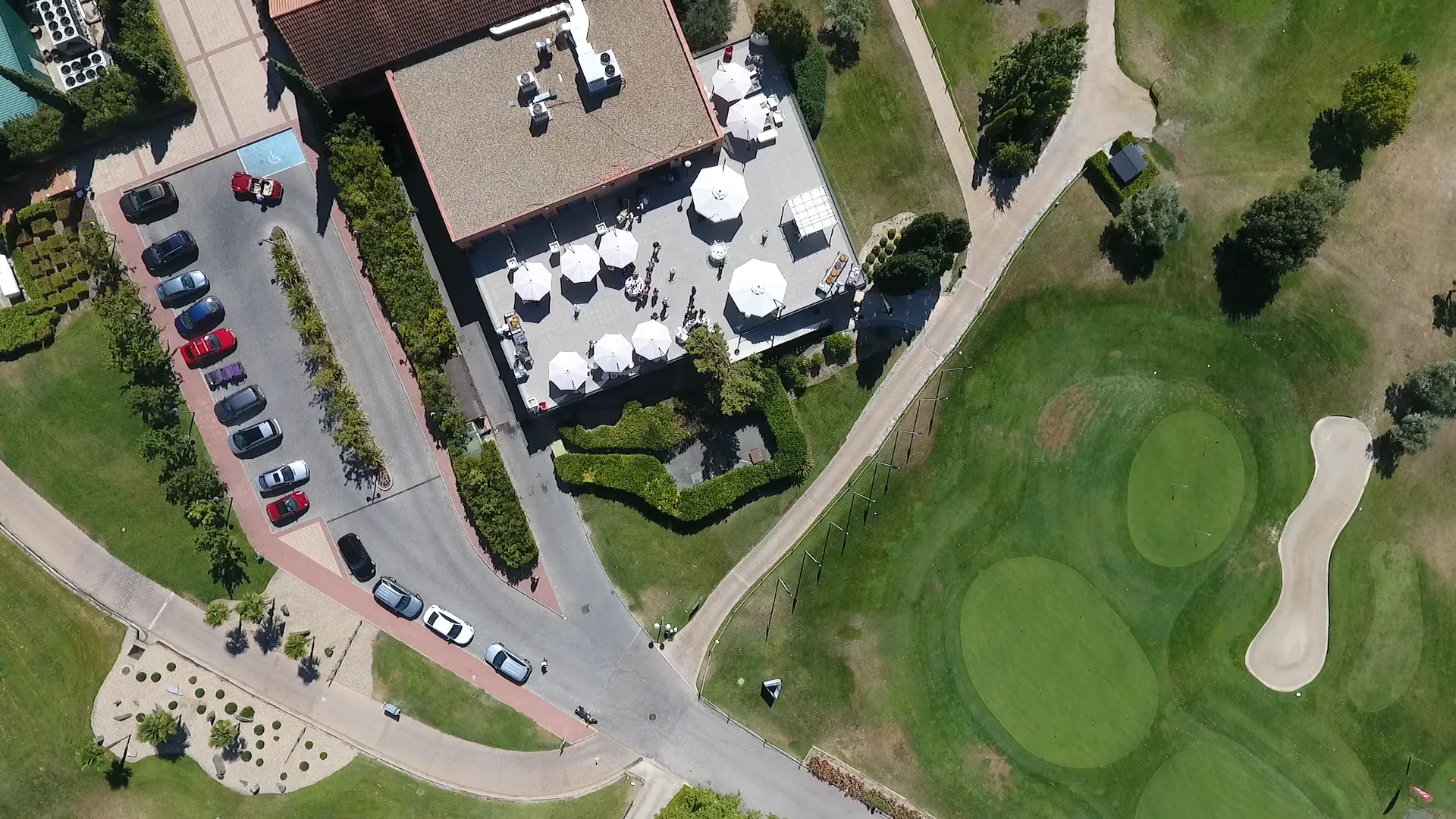 Vista aérea de Retamares Experience con el edificio principal, su terraza con sombrillas y el campo de golf.