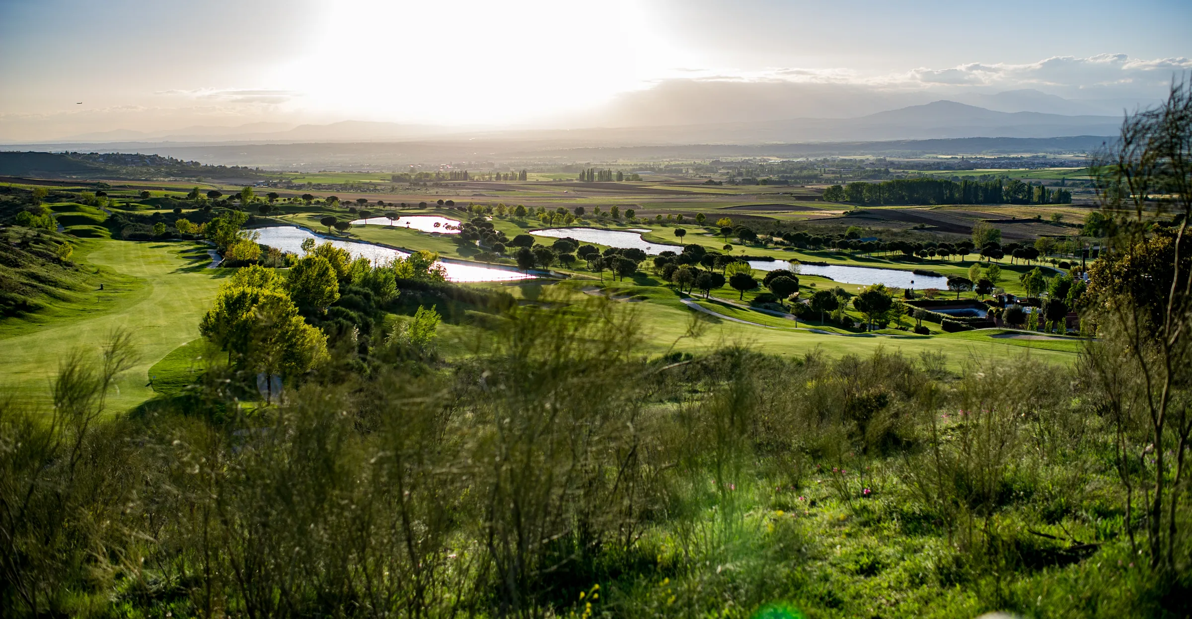 Vista panorámica del campo de golf con lagos y la sierra al fondo en Retamares Experience.