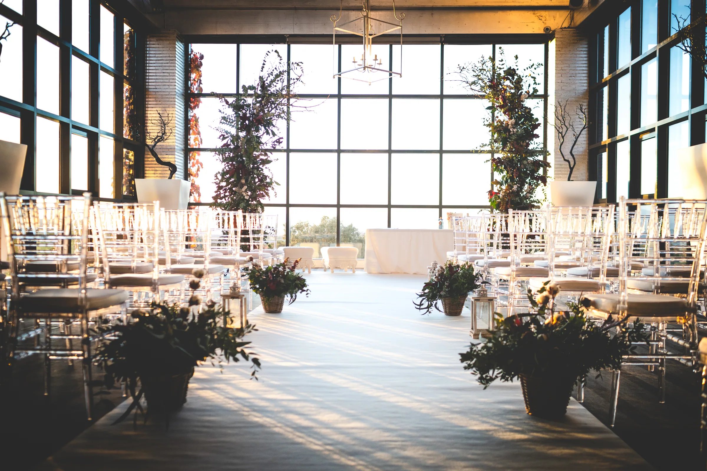 Salón interior preparado para la ceremonia con grandes ventanales y sillas transparentes en Retamares Experience.