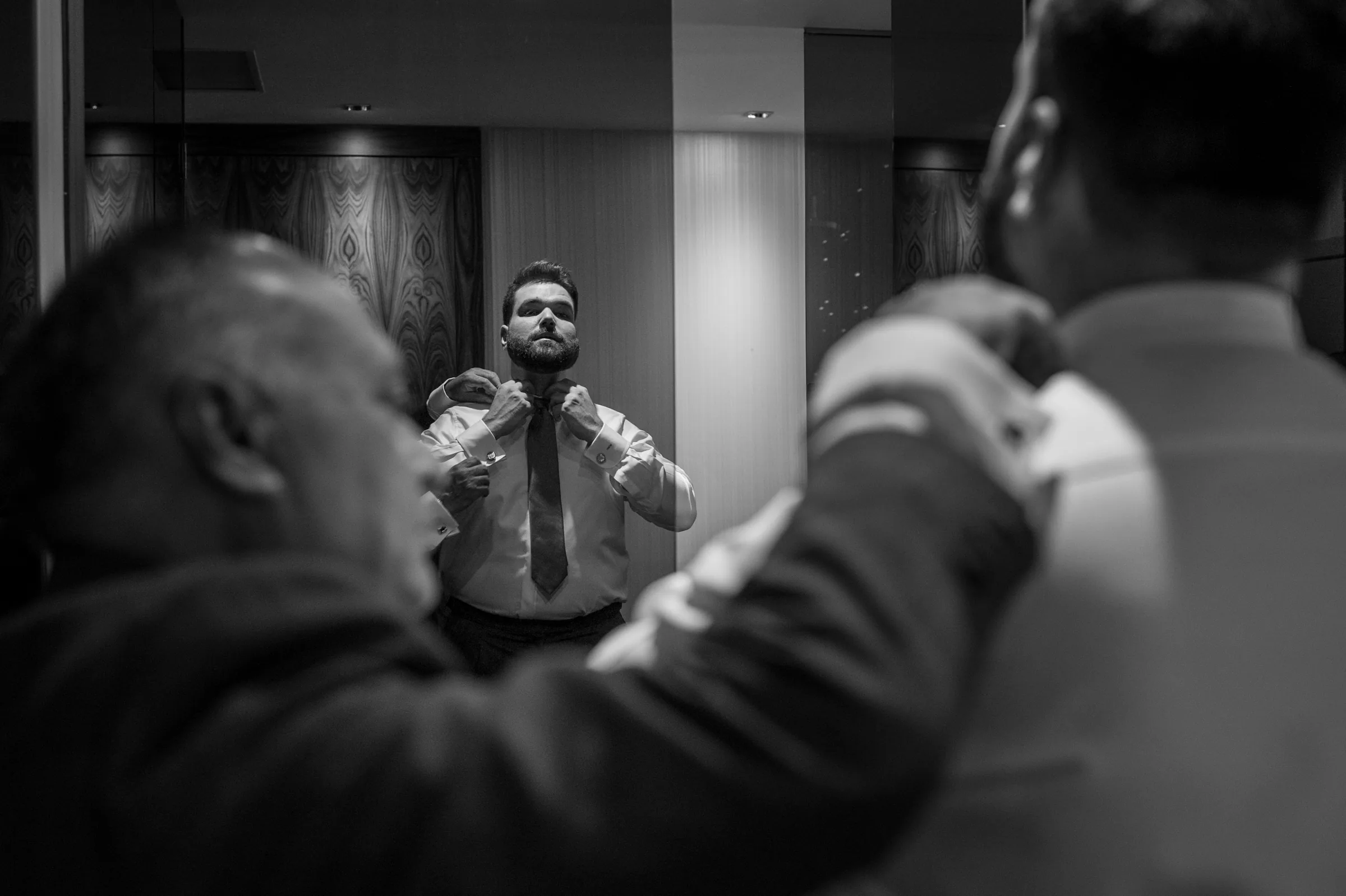 Novio ajustándose la corbata con ayuda de un familiar en blanco y negro en Retamares Experience.