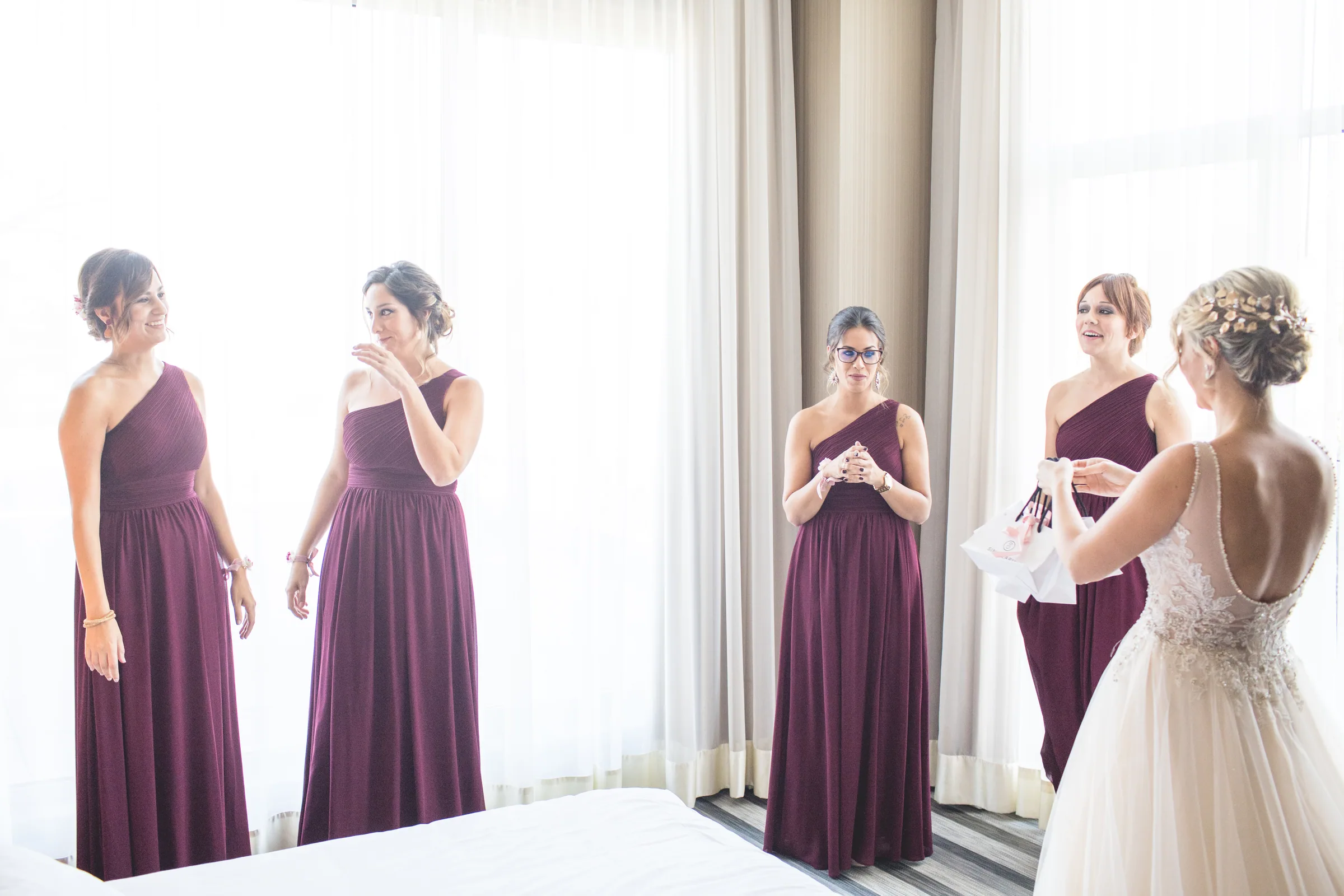 La novia con sus damas de honor junto al gran ventanal de la habitación en Retamares Experience.