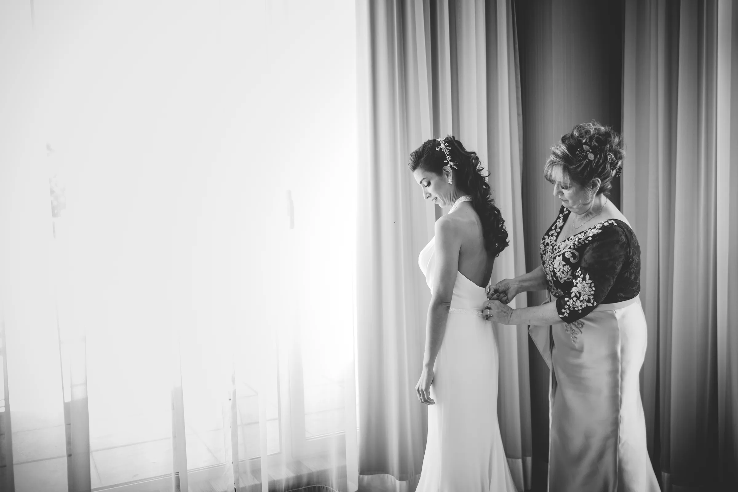 La madre ayuda a la novia con los botones del vestido en blanco y negro en Retamares Experience.