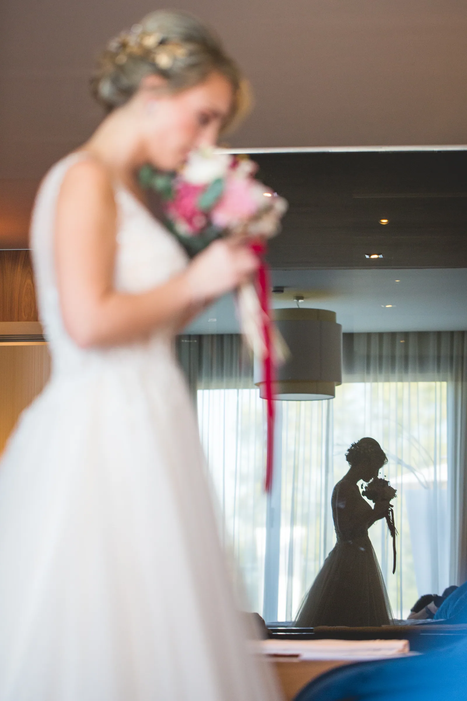 La novia con su ramo de flores junto al ventanal de la habitación en Retamares Experience.