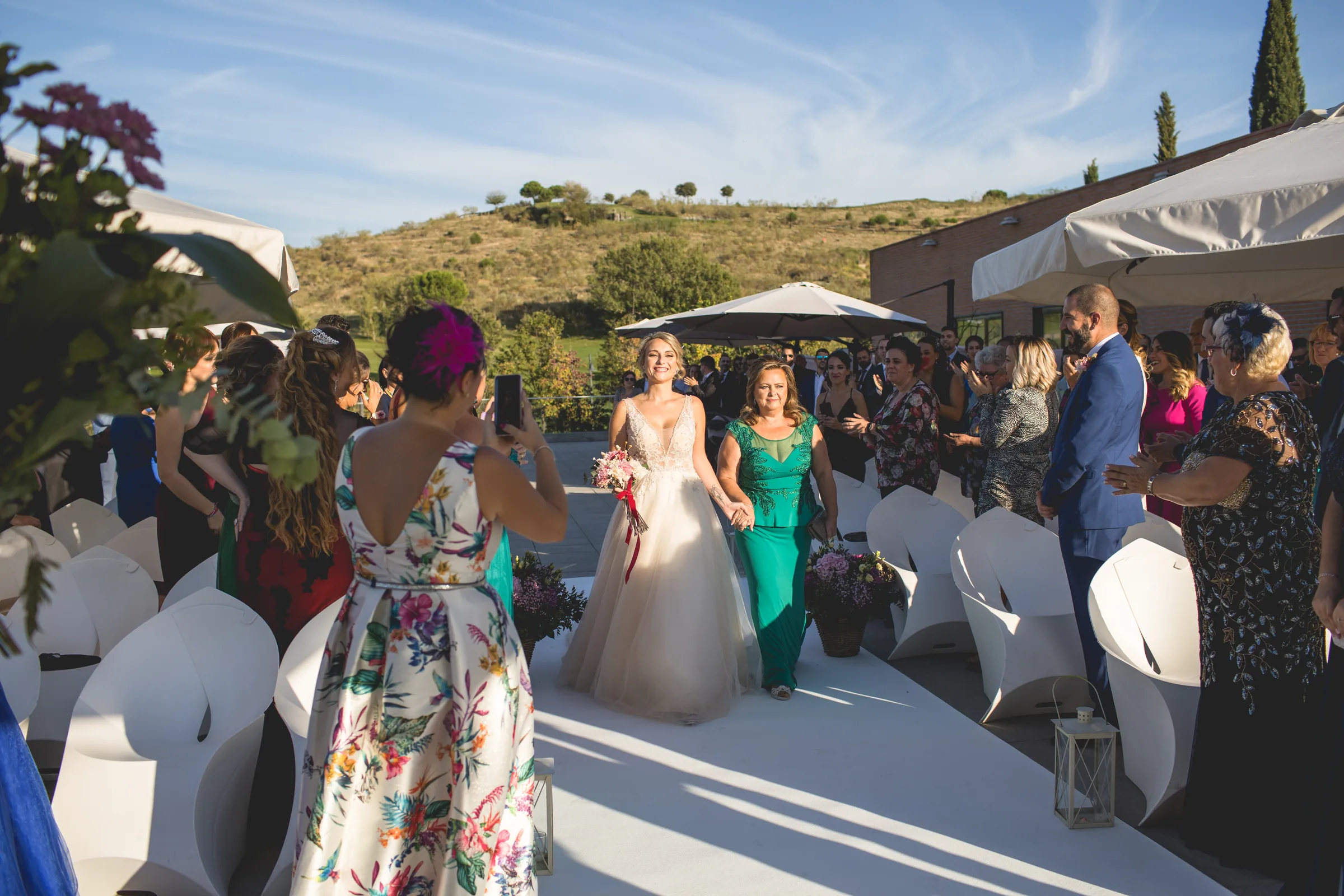 La novia avanza hacia la ceremonia entre invitados y sombrillas blancas en Retamares Experience.