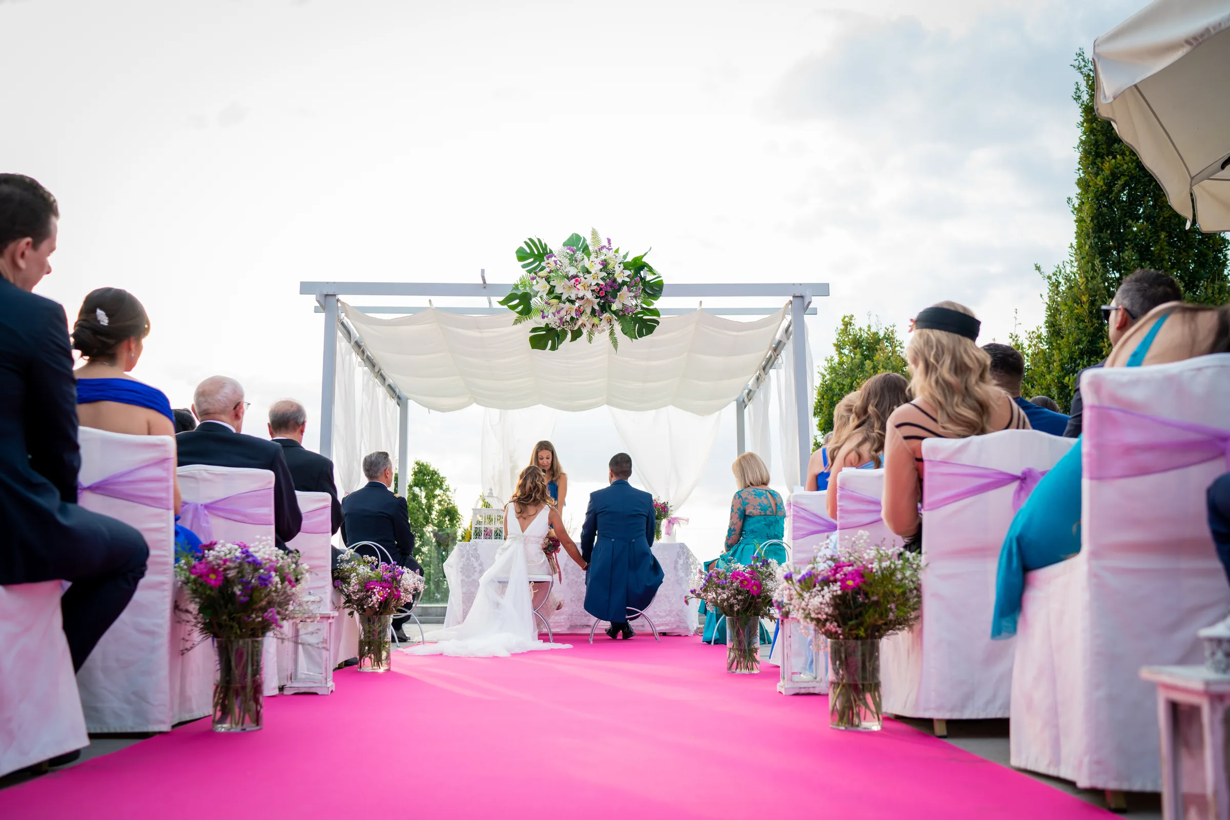 Ceremonia civil bajo un pabellón con arreglo floral y pasillo fucsia, con los invitados sentados en Retamares Experience.