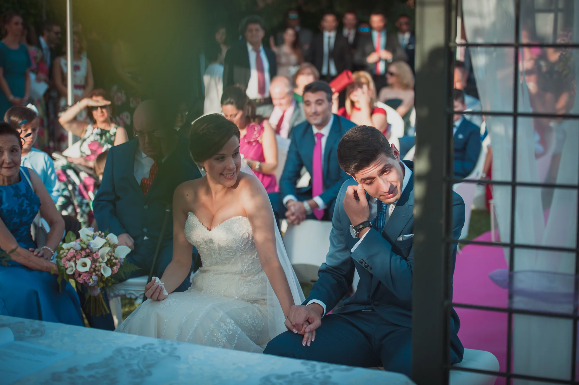 Los novios sonríen emocionados durante la ceremonia con los invitados detrás en Retamares Experience.