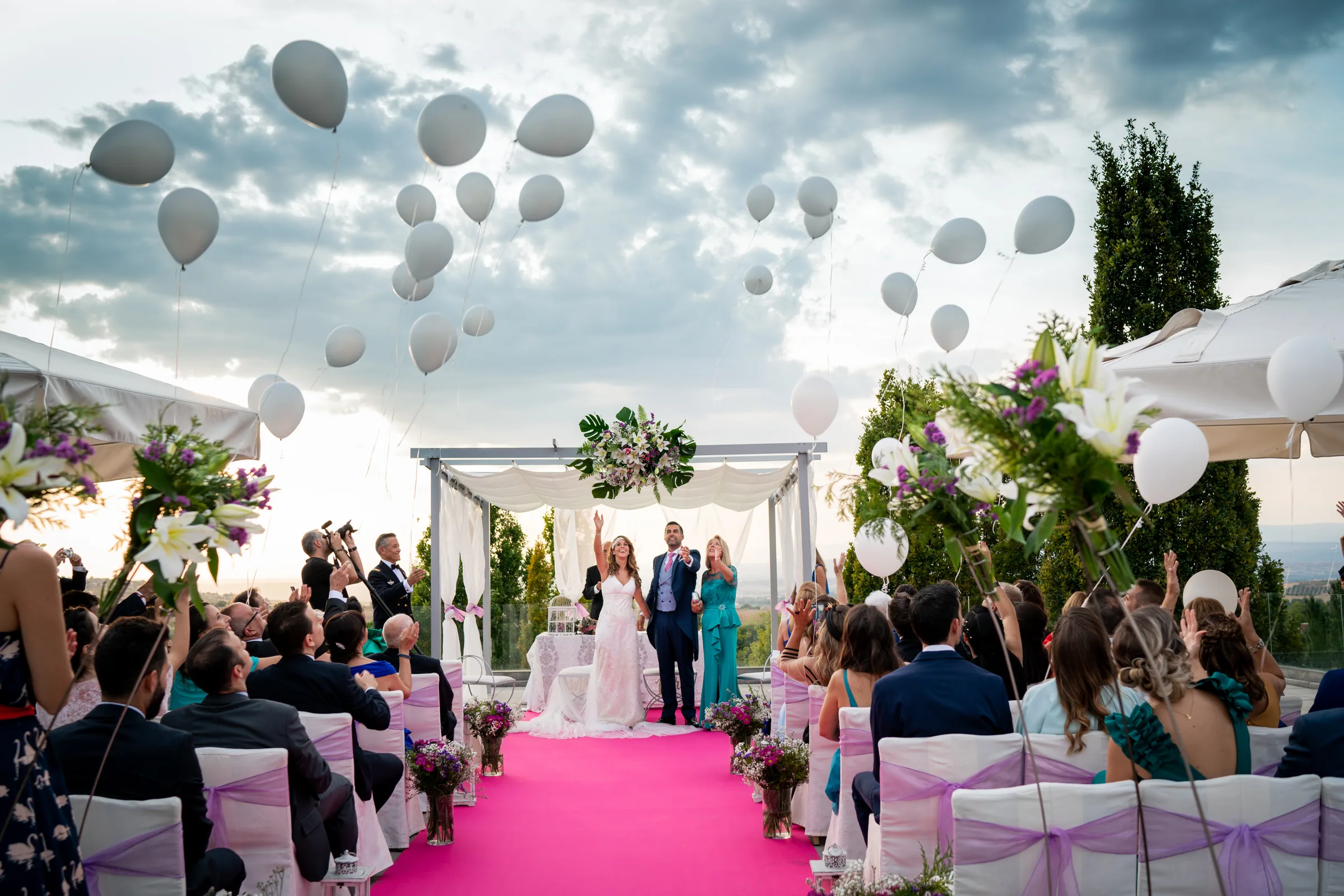 Suelta de globos blancos sobre la ceremonia al aire libre, con el pasillo fucsia y el pabellón de flores en Retamares Experience.