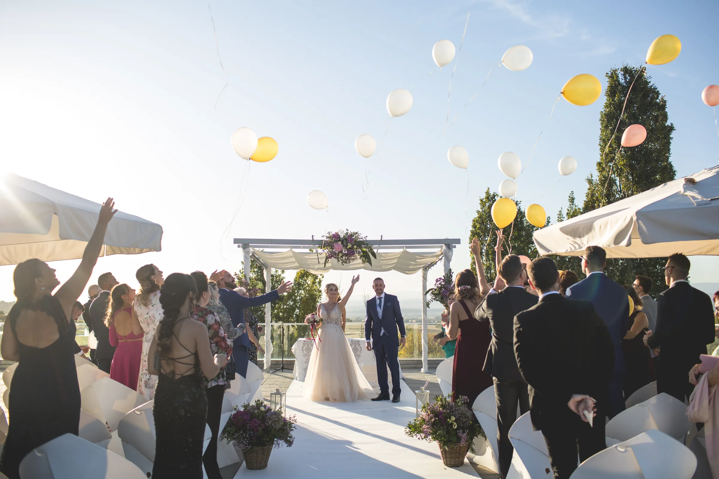 Los invitados lanzan globos mientras los novios salen de la ceremonia bajo el pabellón en Retamares Experience.