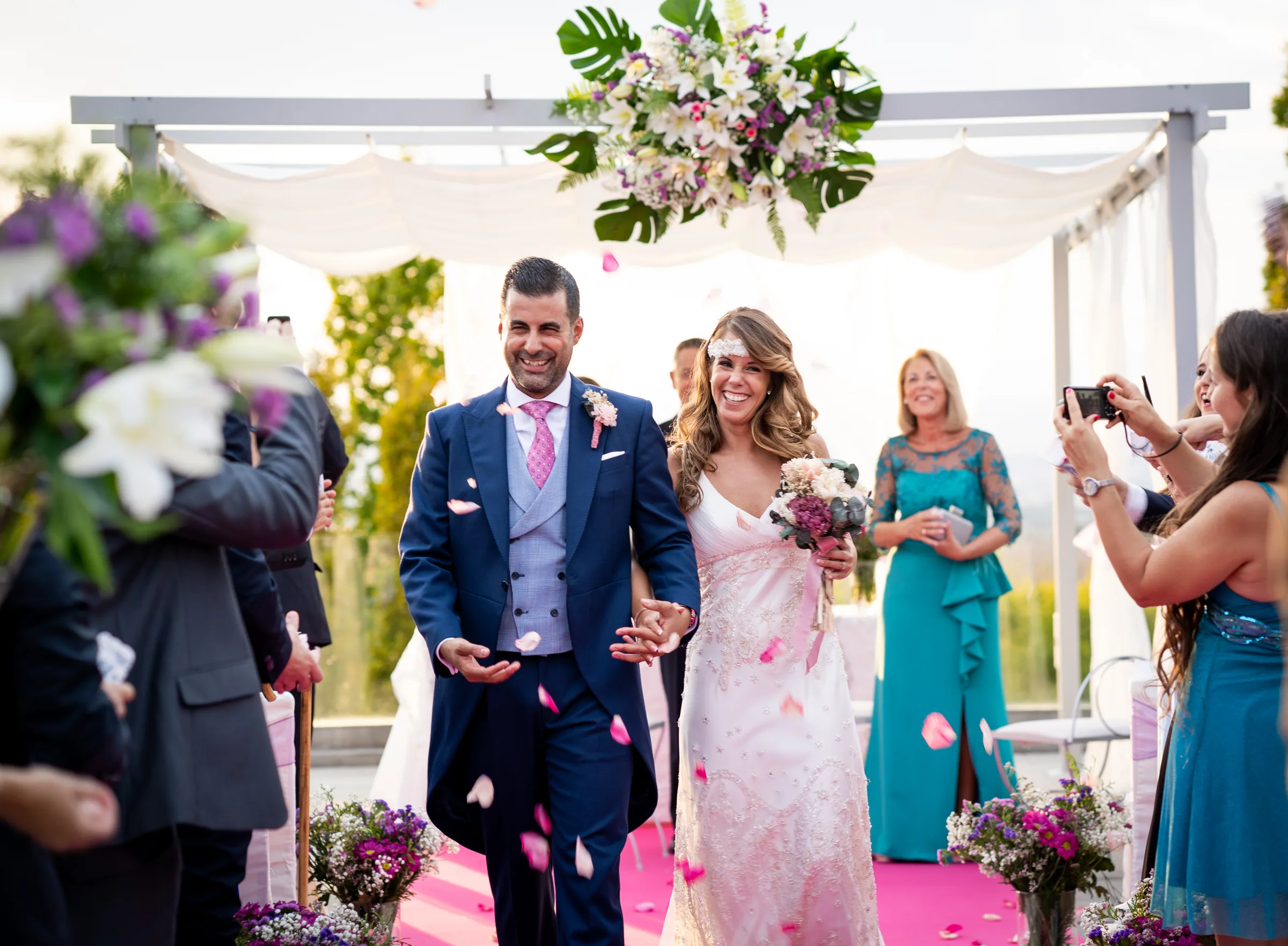 Los novios salen de la ceremonia entre una lluvia de pétalos mientras los invitados los fotografían en Retamares Experience.