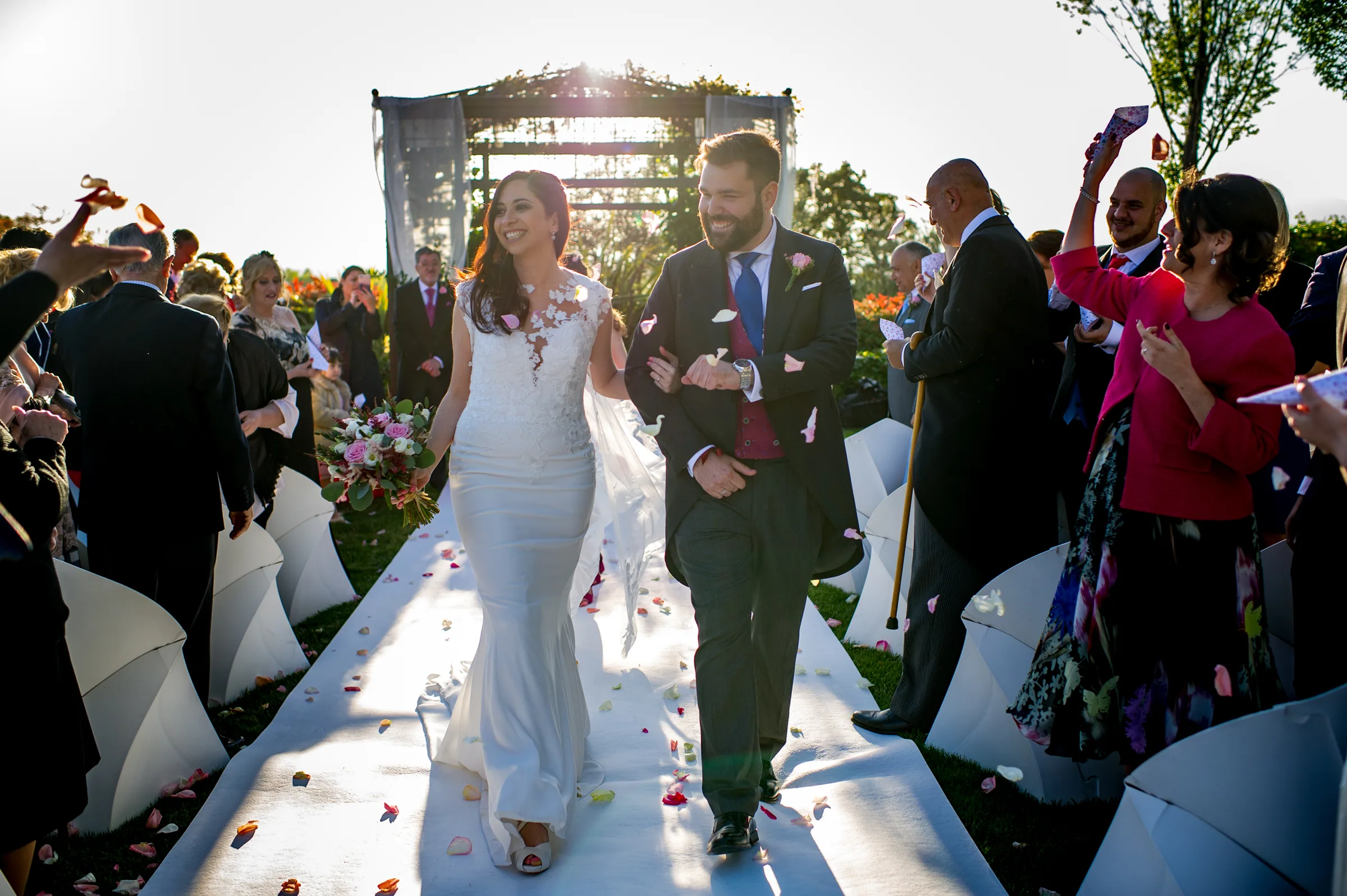 Los novios salen de la ceremonia por un pasillo blanco entre invitados que lanzan pétalos en Retamares Experience.
