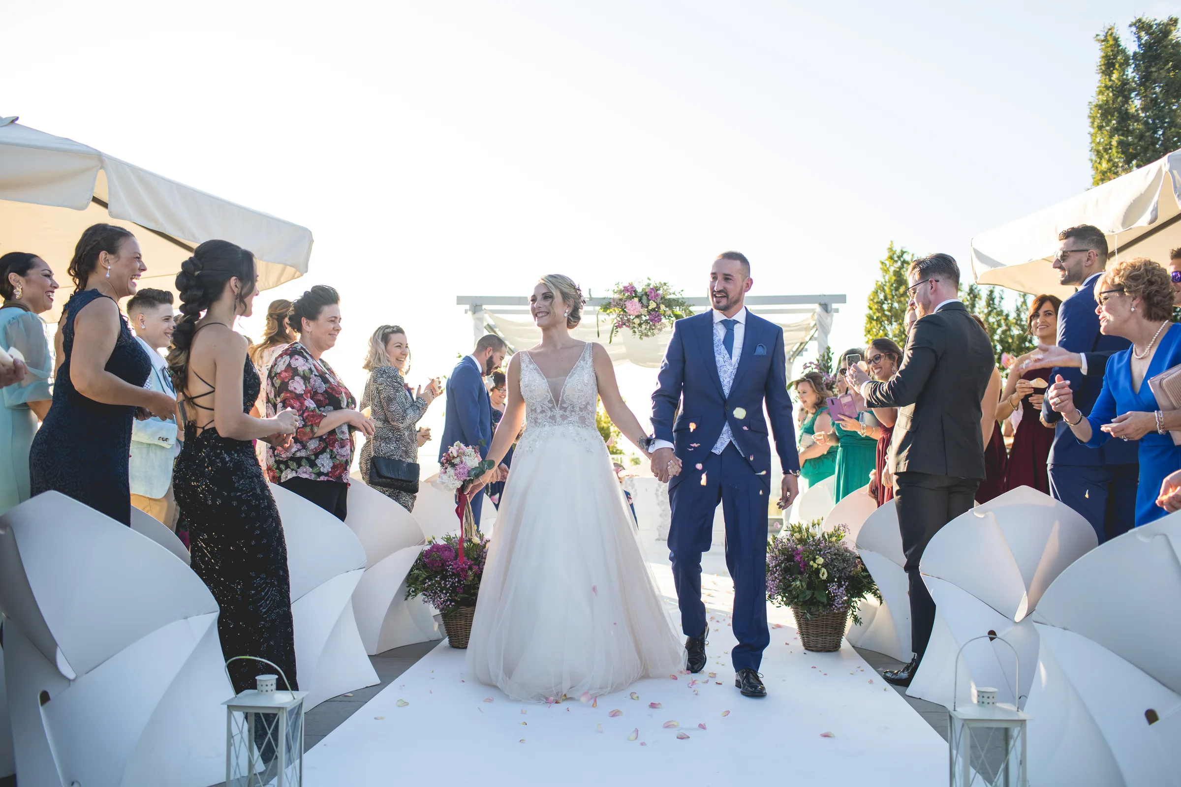 Los novios salen de la ceremonia entre invitados y sombrillas blancas en Retamares Experience.