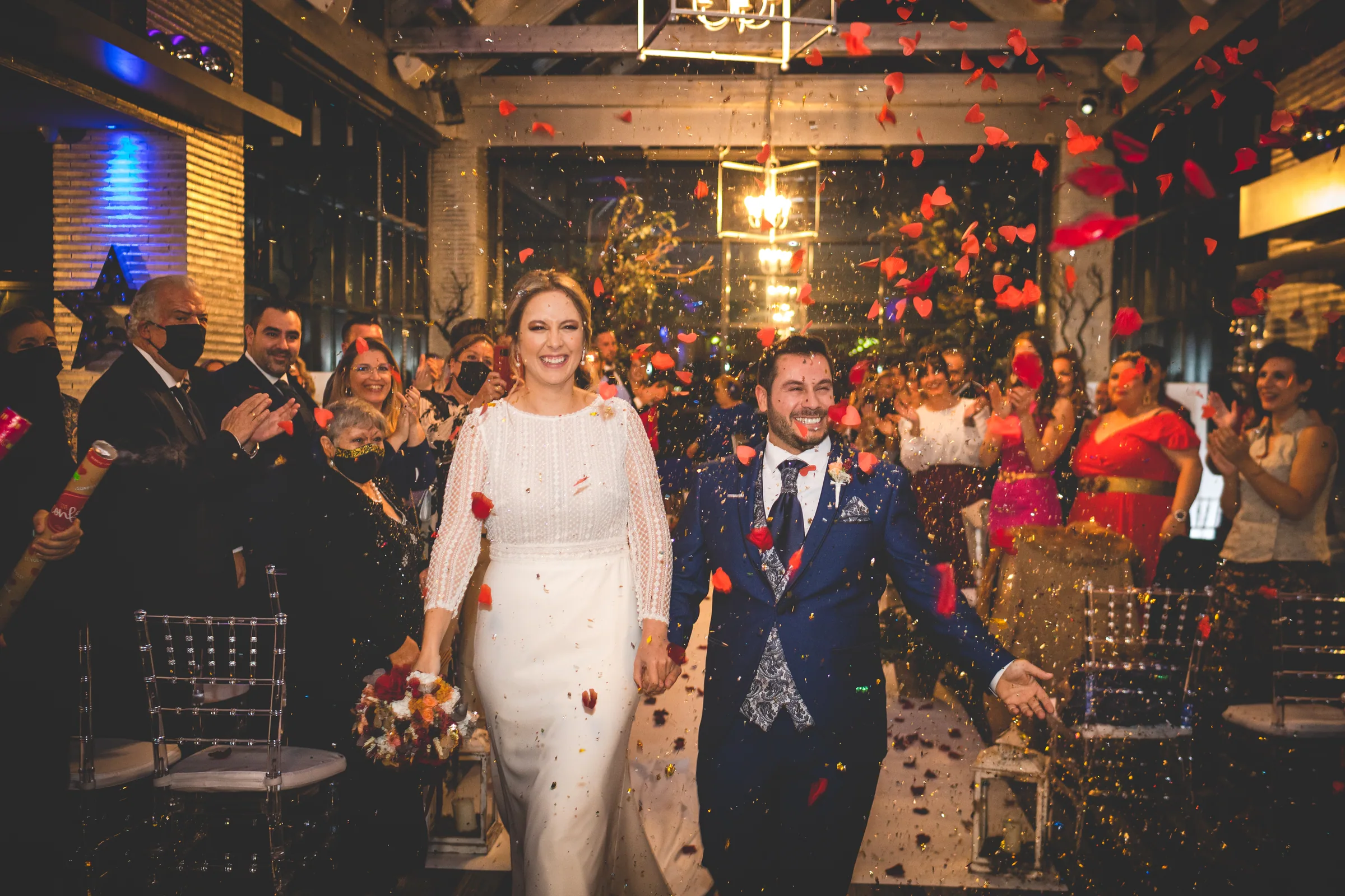 Los novios avanzan de la mano entre pétalos rojos y los aplausos de los invitados en Retamares Experience.