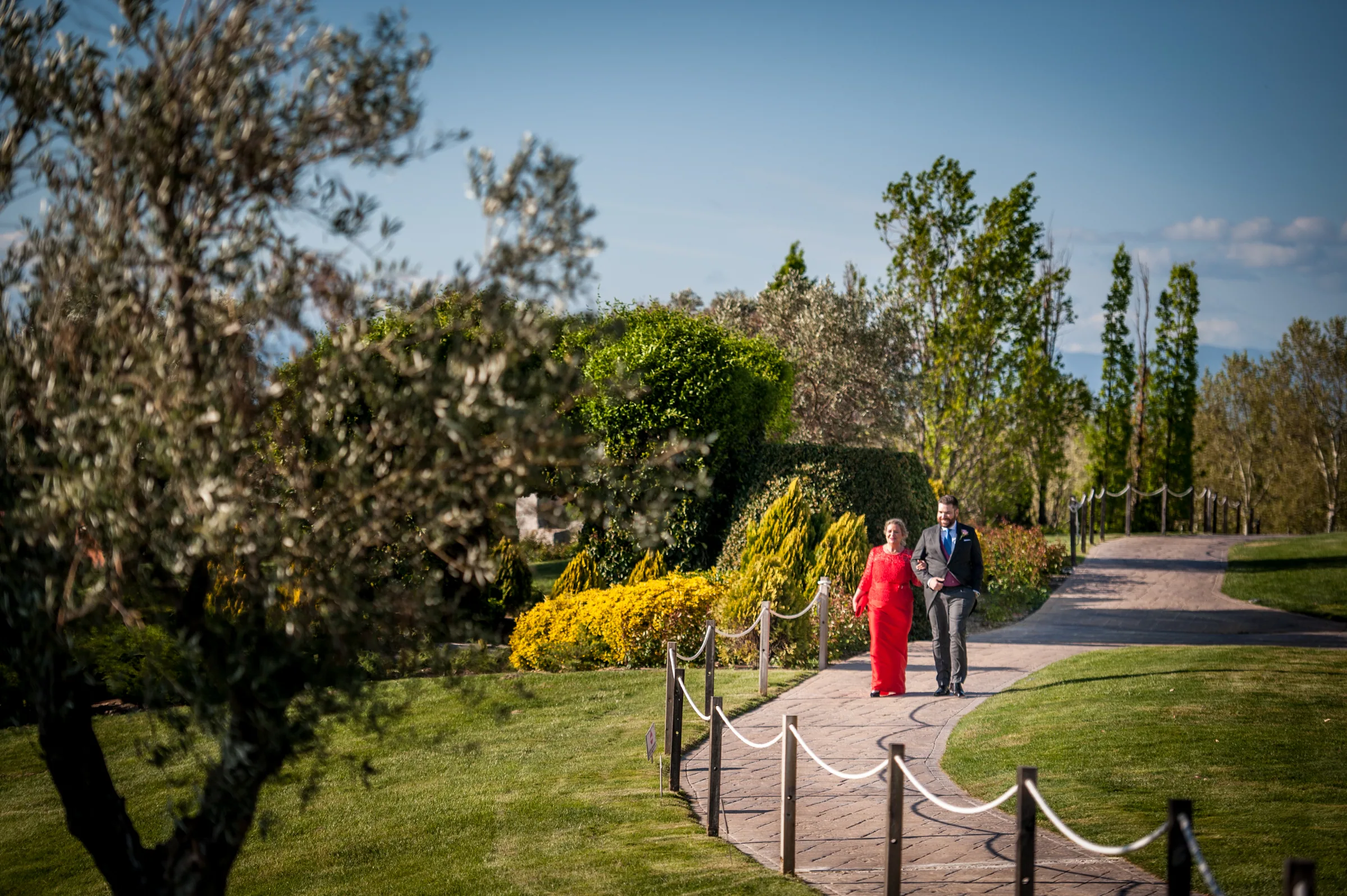 Invitados pasean por un camino ajardinado de la finca entre arbustos y árboles en Retamares Experience.
