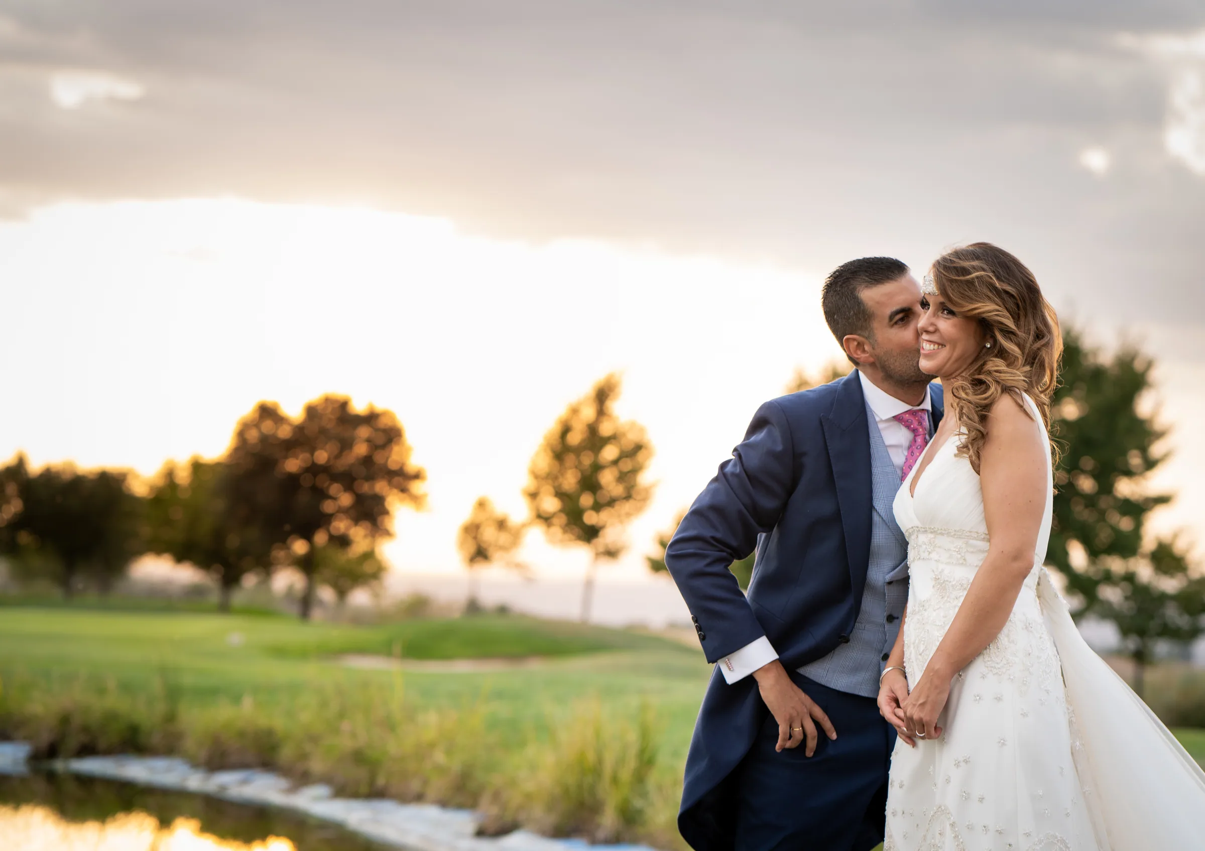 Los novios se abrazan y sonríen al atardecer junto al lago en Retamares Experience.