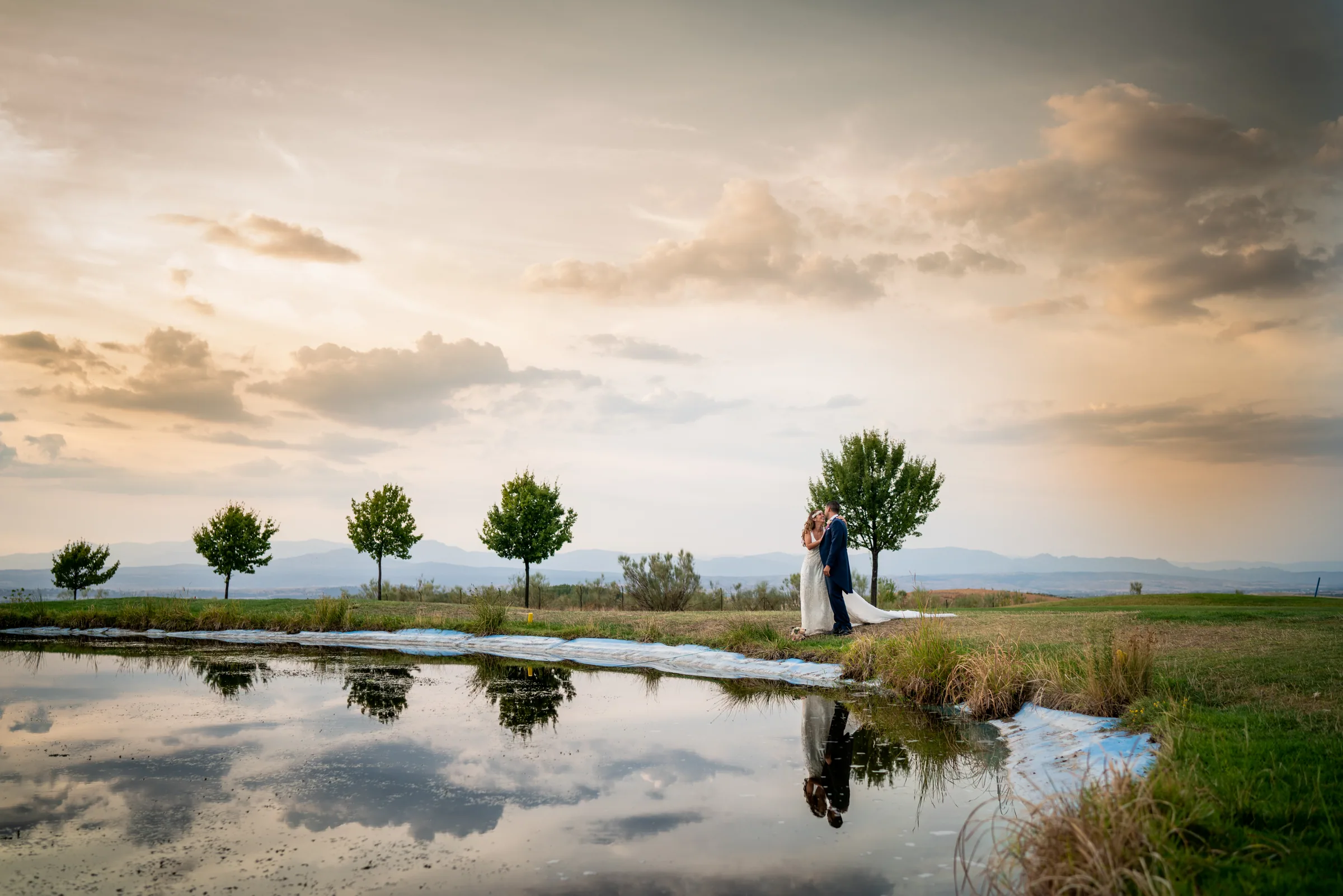 Los novios reflejados en el lago al atardecer en Retamares Experience