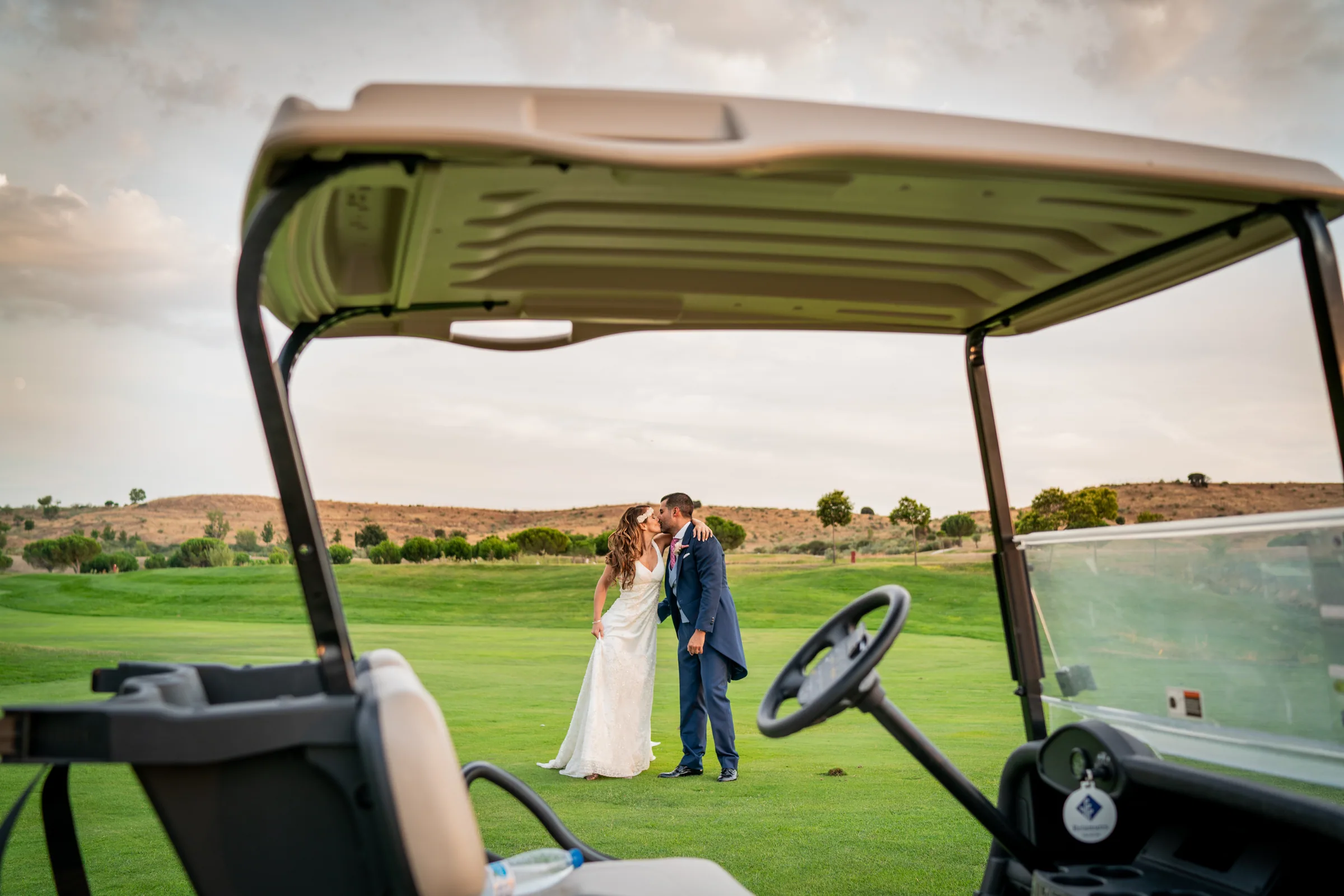 Los novios se besan junto a un buggy de golf en el campo en Retamares Experience.