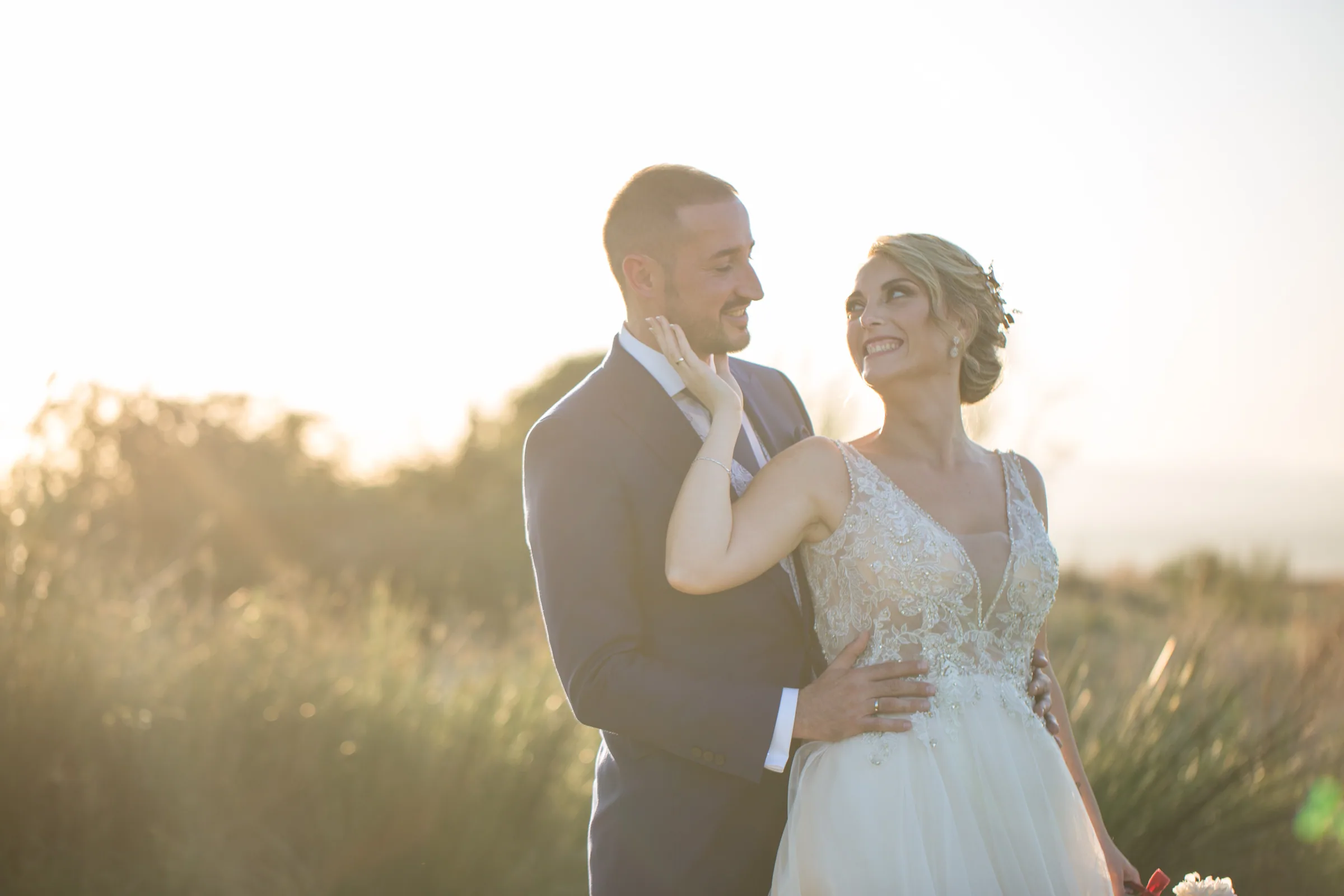 Los novios se abrazan con luz de atardecer mientras ella mira hacia arriba en Retamares Experience.