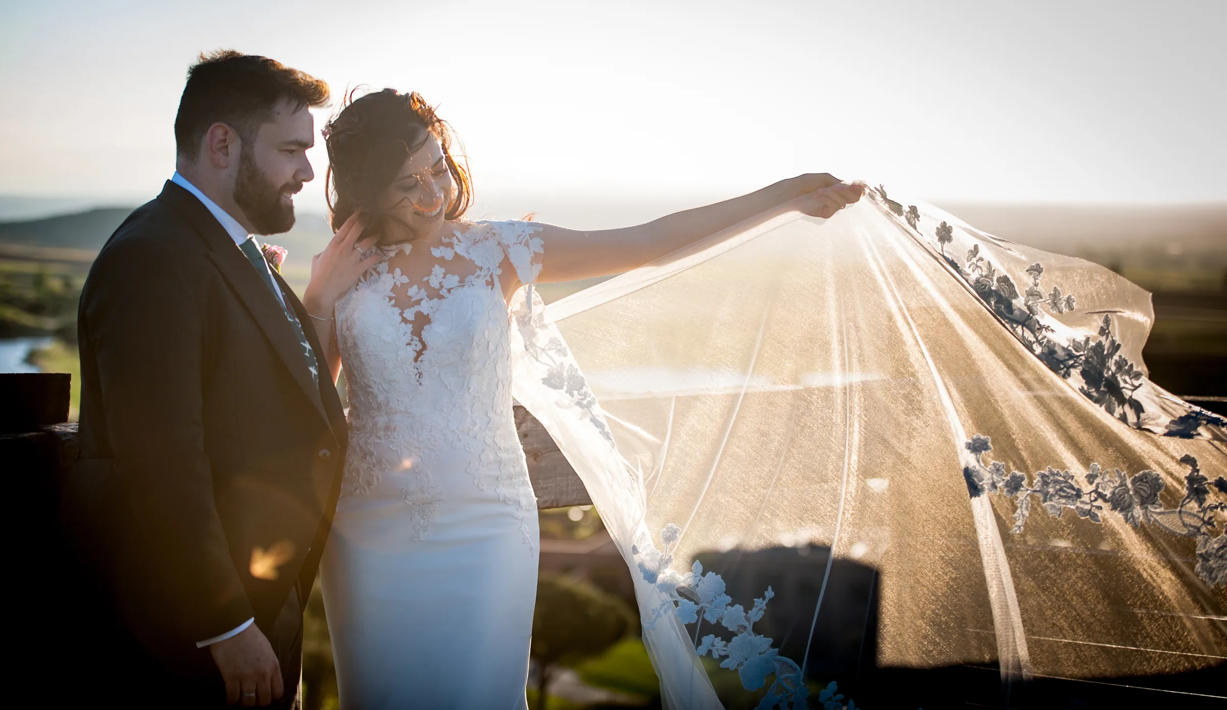 Los novios abrazados bajo el velo de la novia levantado a contraluz en Retamares Experience.