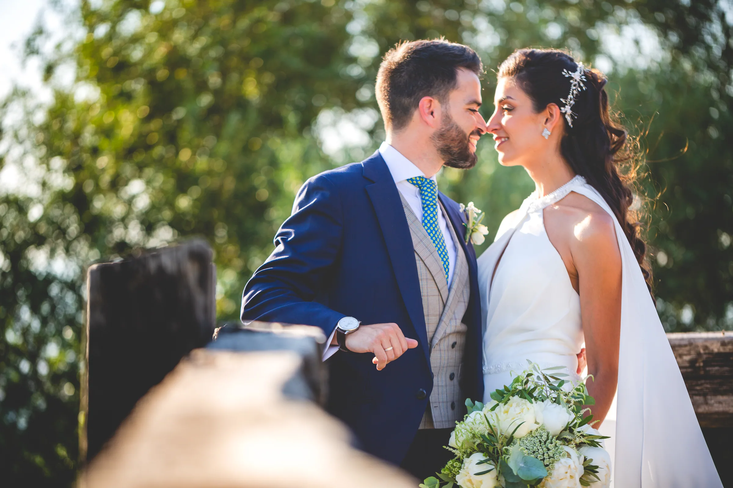 Retrato de los novios cara a cara con el ramo de flores blancas entre vegetación en Retamares Experience.