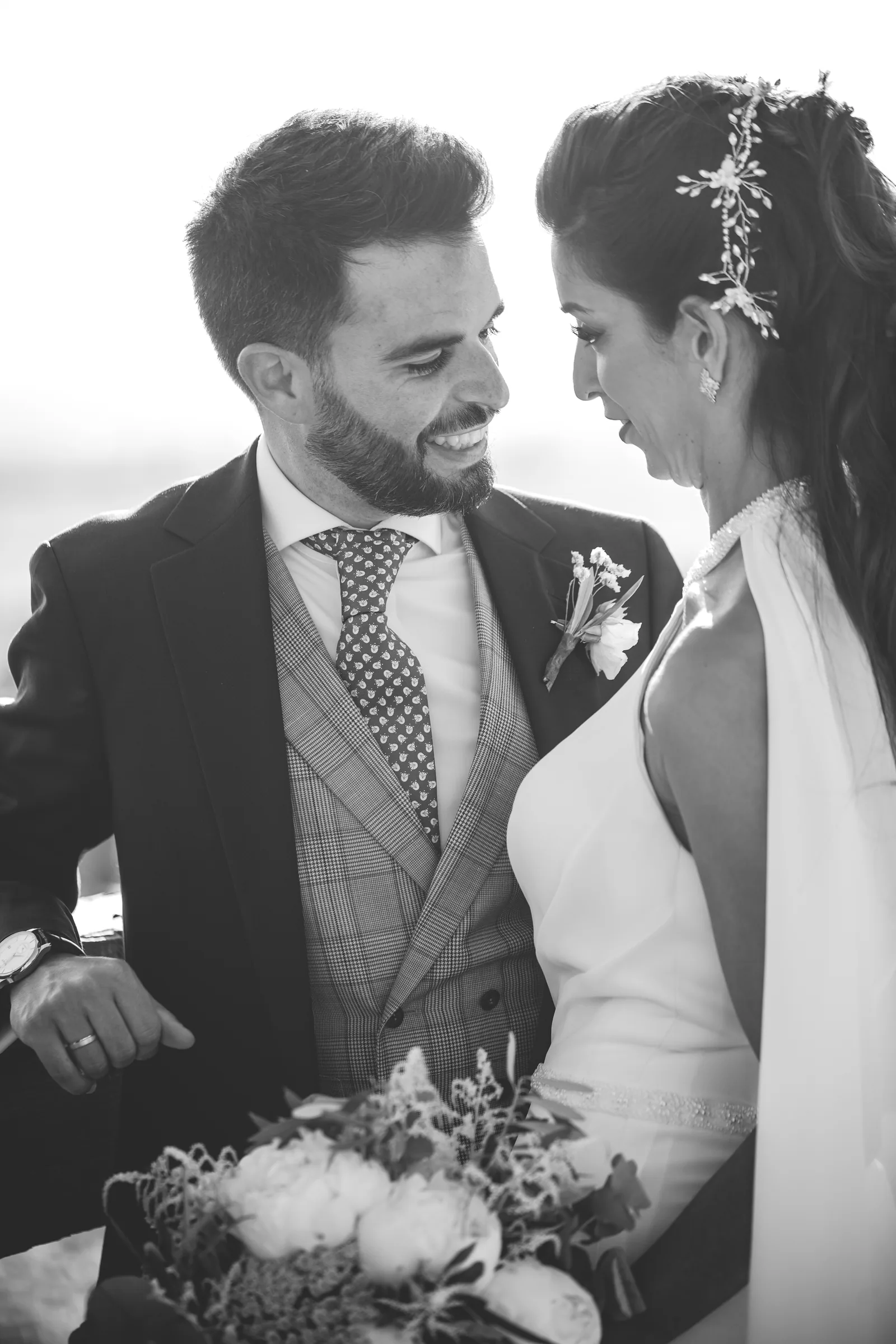 Los novios se miran sonrientes con el ramo en blanco y negro en Retamares Experience.