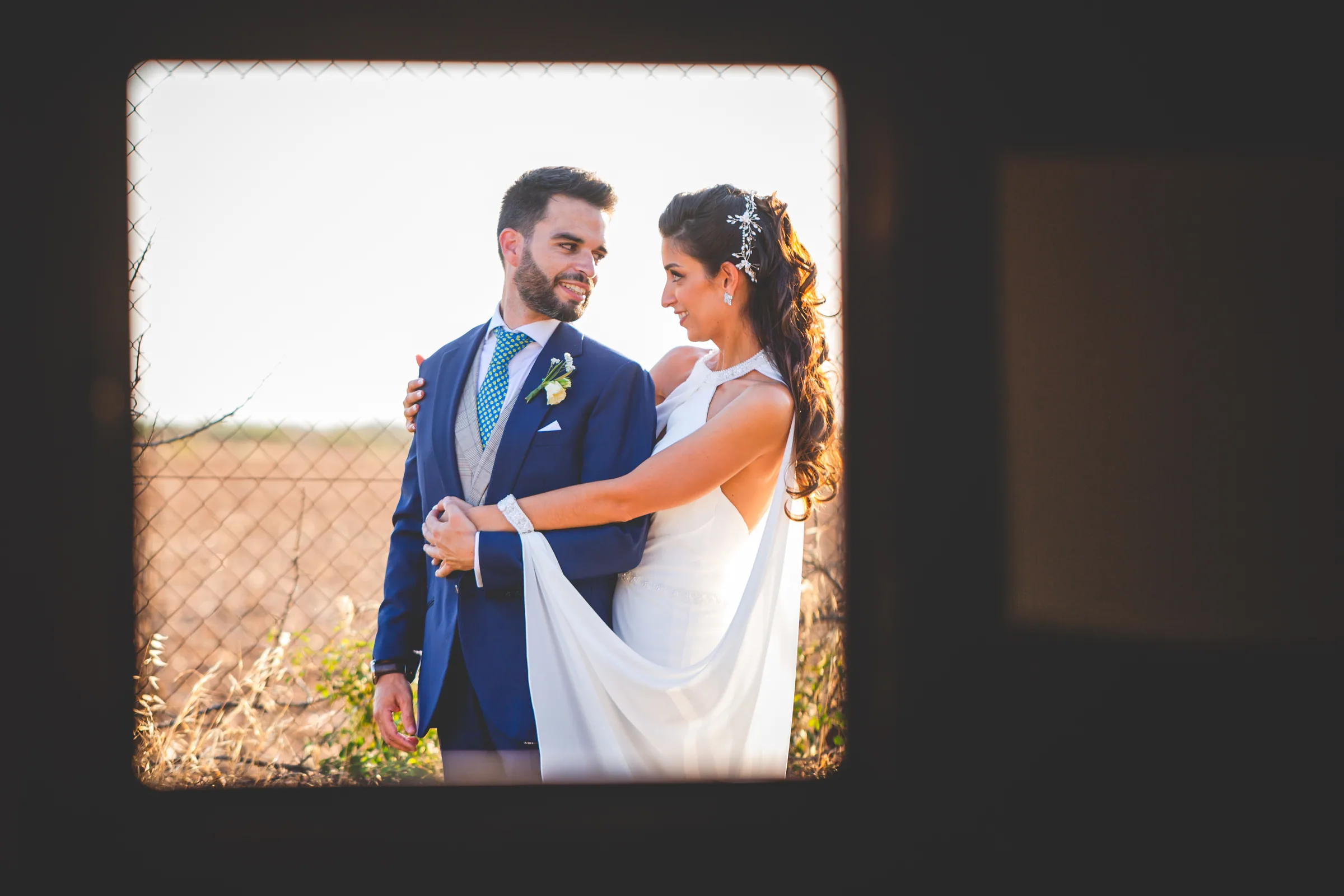 Los novios enmarcados por una ventana oscura con el campo de fondo en Retamares Experience.