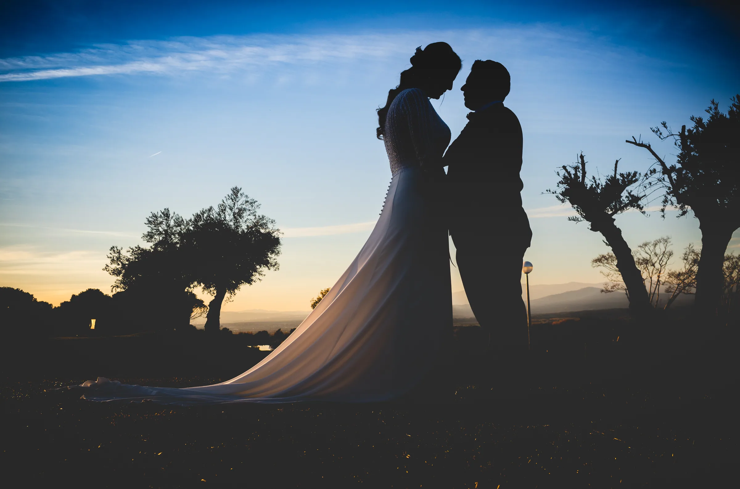 Silueta de los novios con el velo largo contra el cielo azul del atardecer en Retamares Experience.