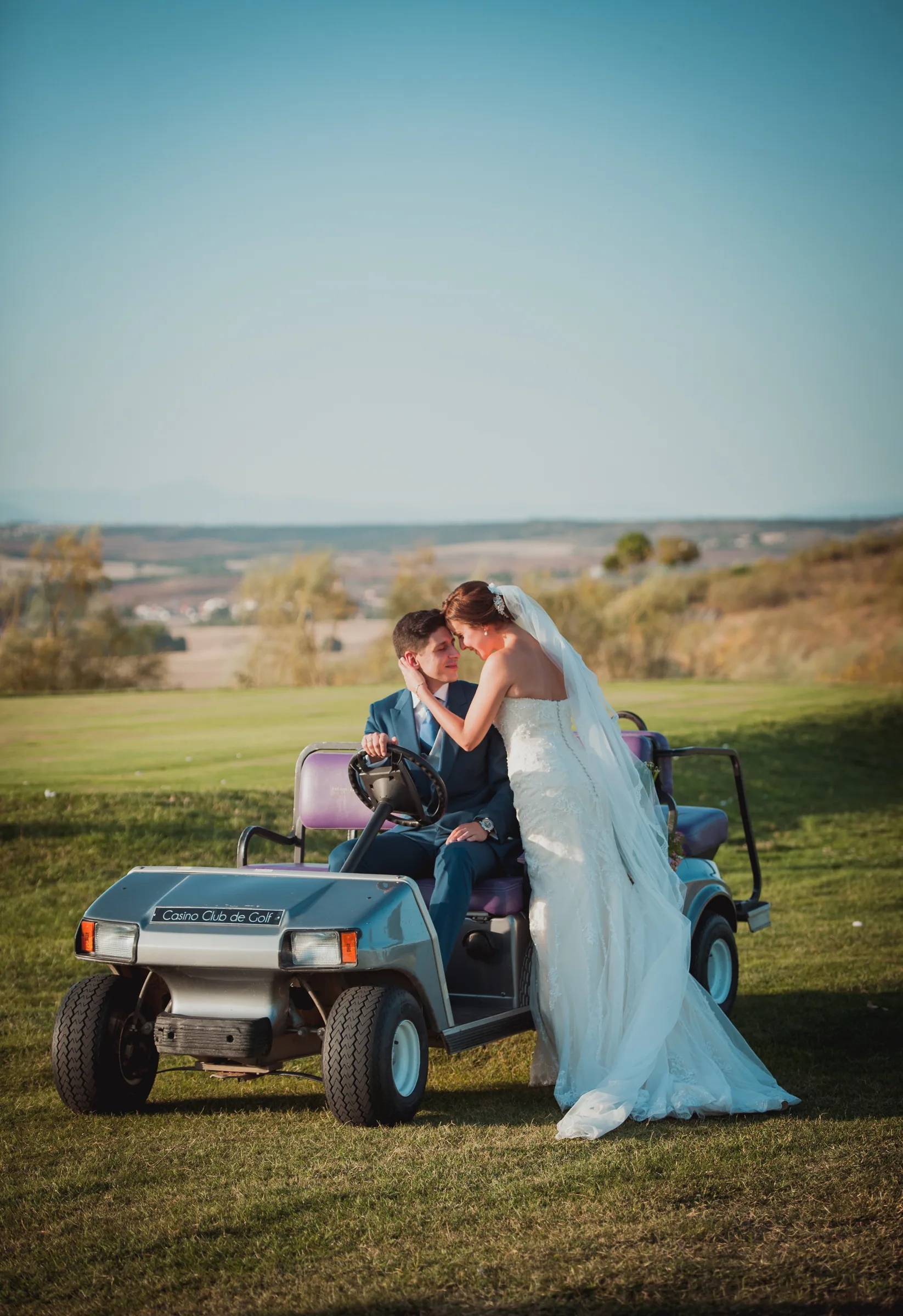 Los novios se besan en un buggy de golf con el campo y el paisaje al fondo en Retamares Experience.