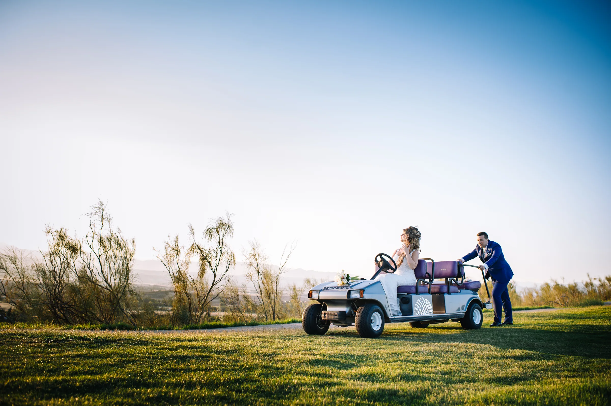 La novia en un buggy de golf mientras el novio la espera junto al campo en Retamares Experience.