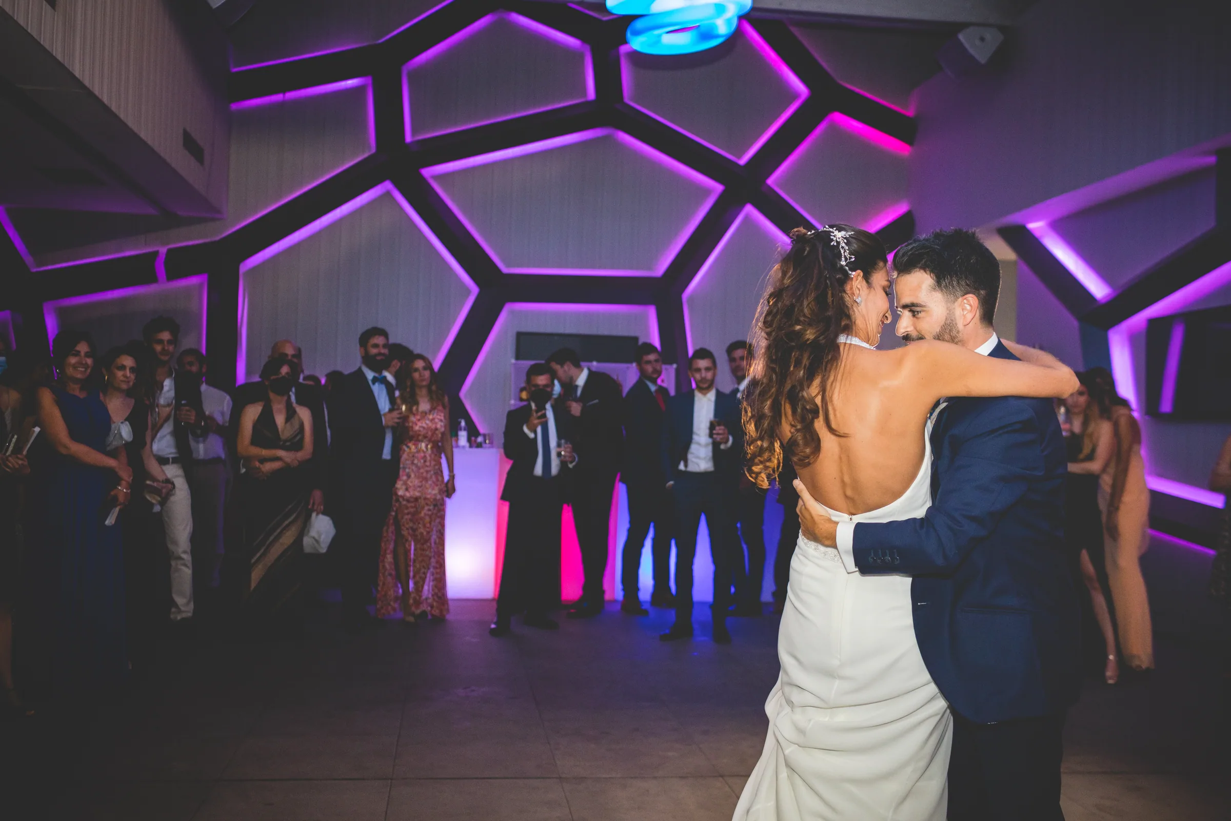 Los novios se abrazan bailando bajo luces moradas geométricas en Retamares Experience.