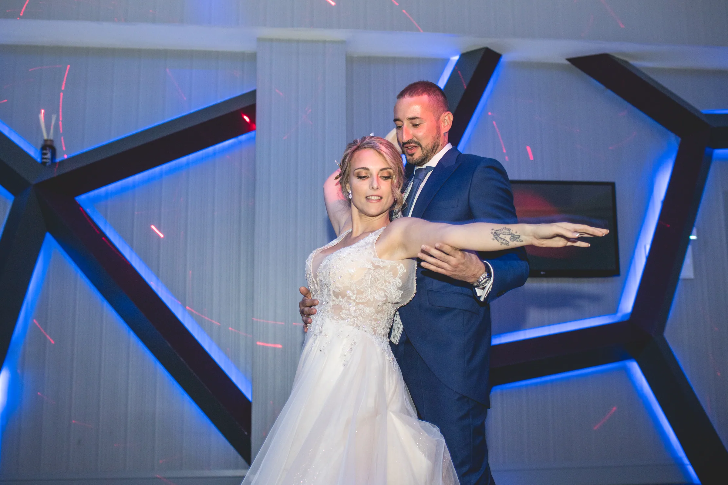 Los novios bailan en la pista con luces azules geométricas en Retamares Experience.
