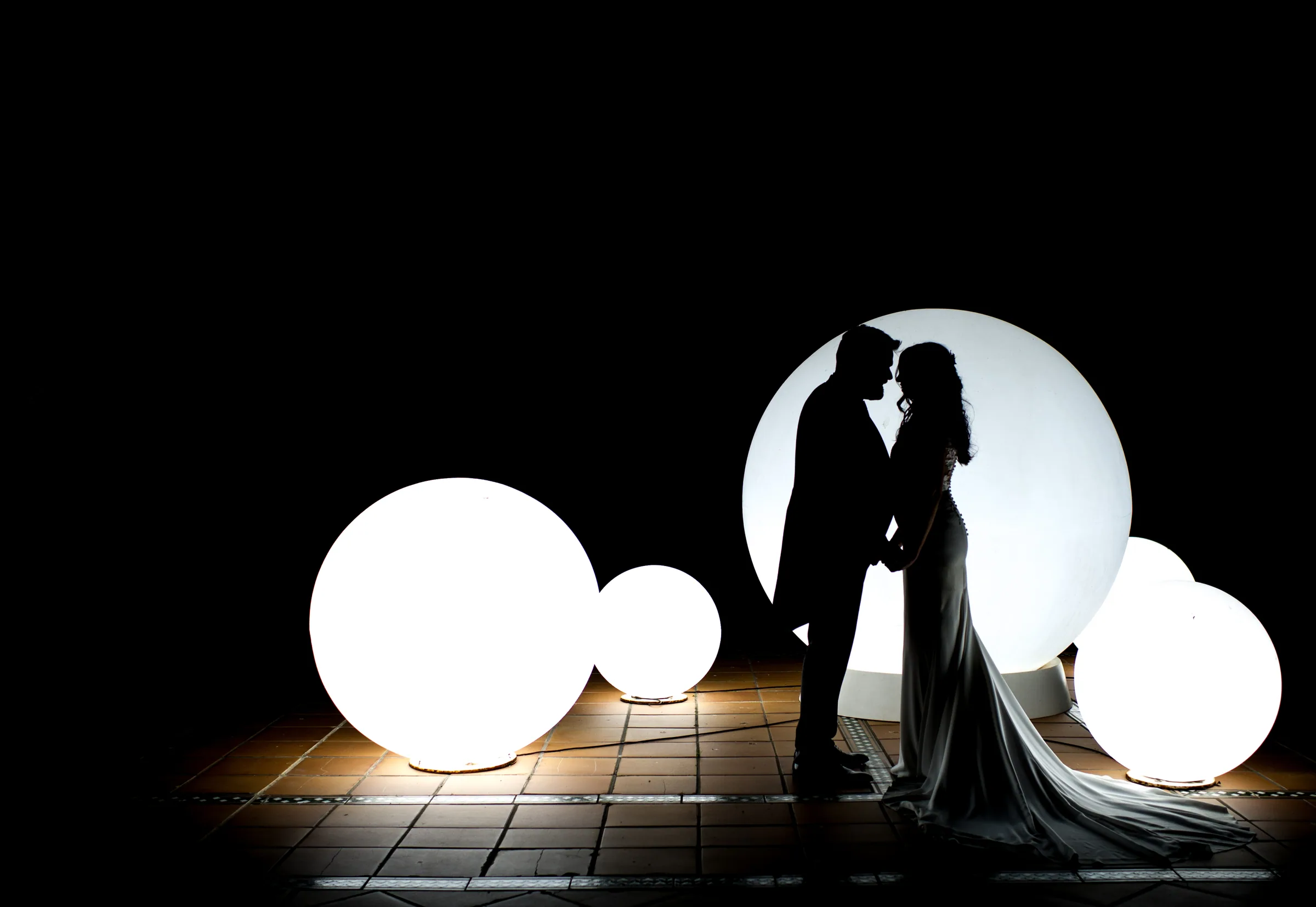 Silueta de los novios frente a grandes esferas luminosas en la sesión nocturna en Retamares Experience.