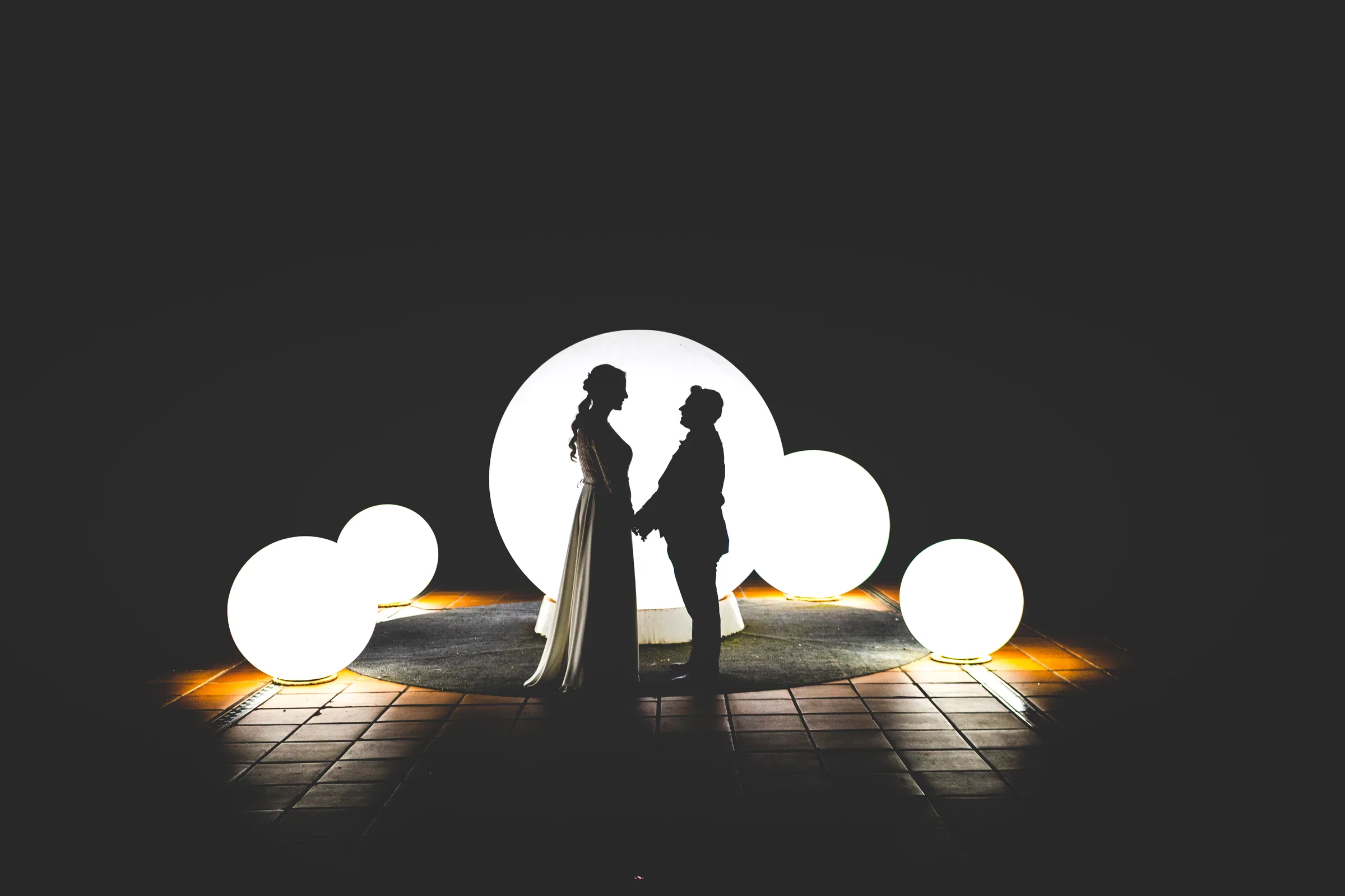Silueta de los novios entre esferas luminosas sobre el suelo en la noche en Retamares Experience.