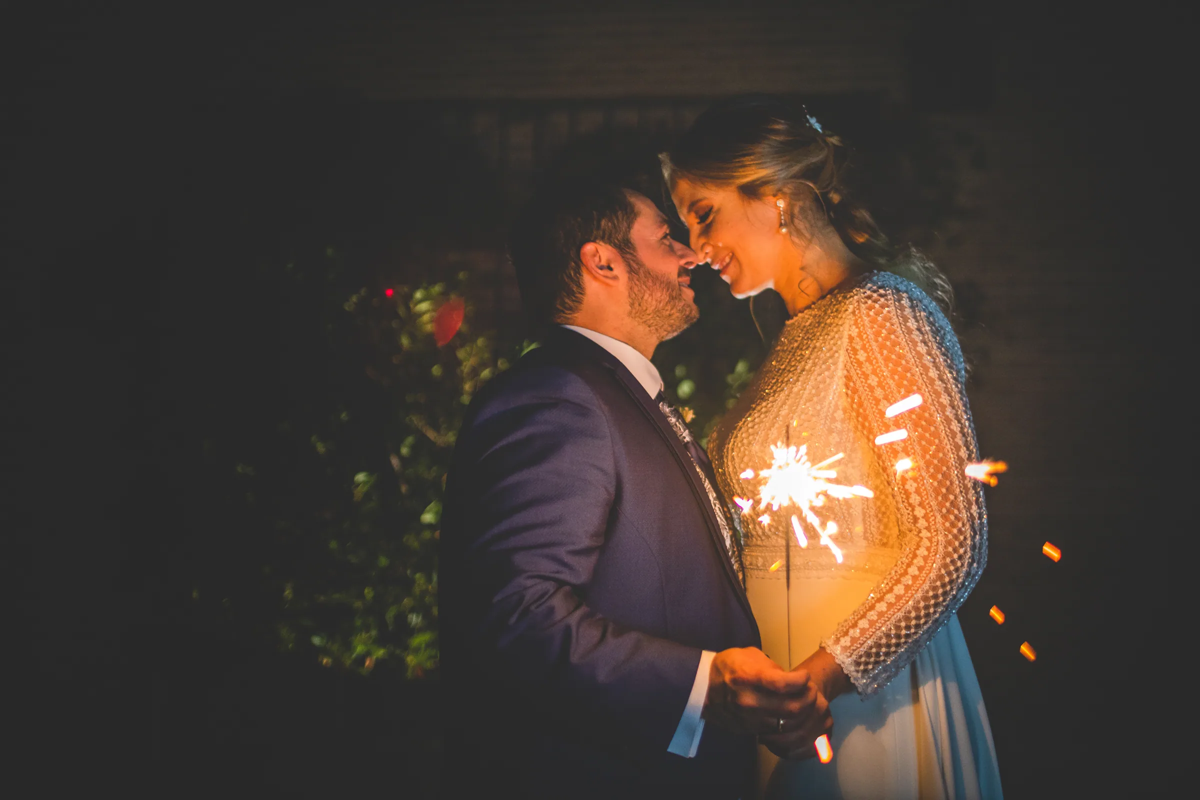 Los novios abrazados con una bengala encendida en la noche en Retamares Experience.