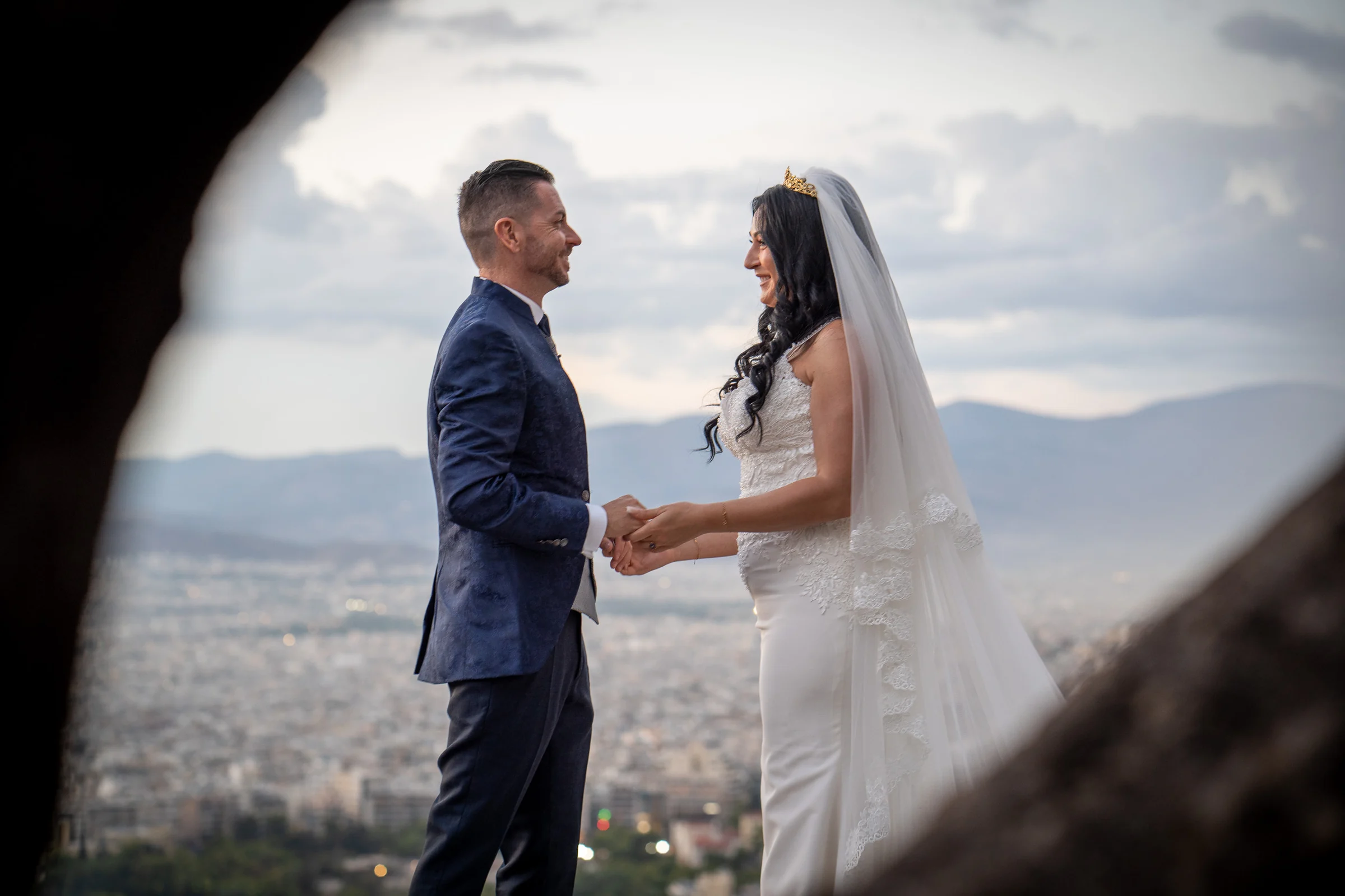 Sara y Edu se miran y se toman de las manos desde un mirador con la ciudad de Atenas al fondo durante su postboda en Grecia.