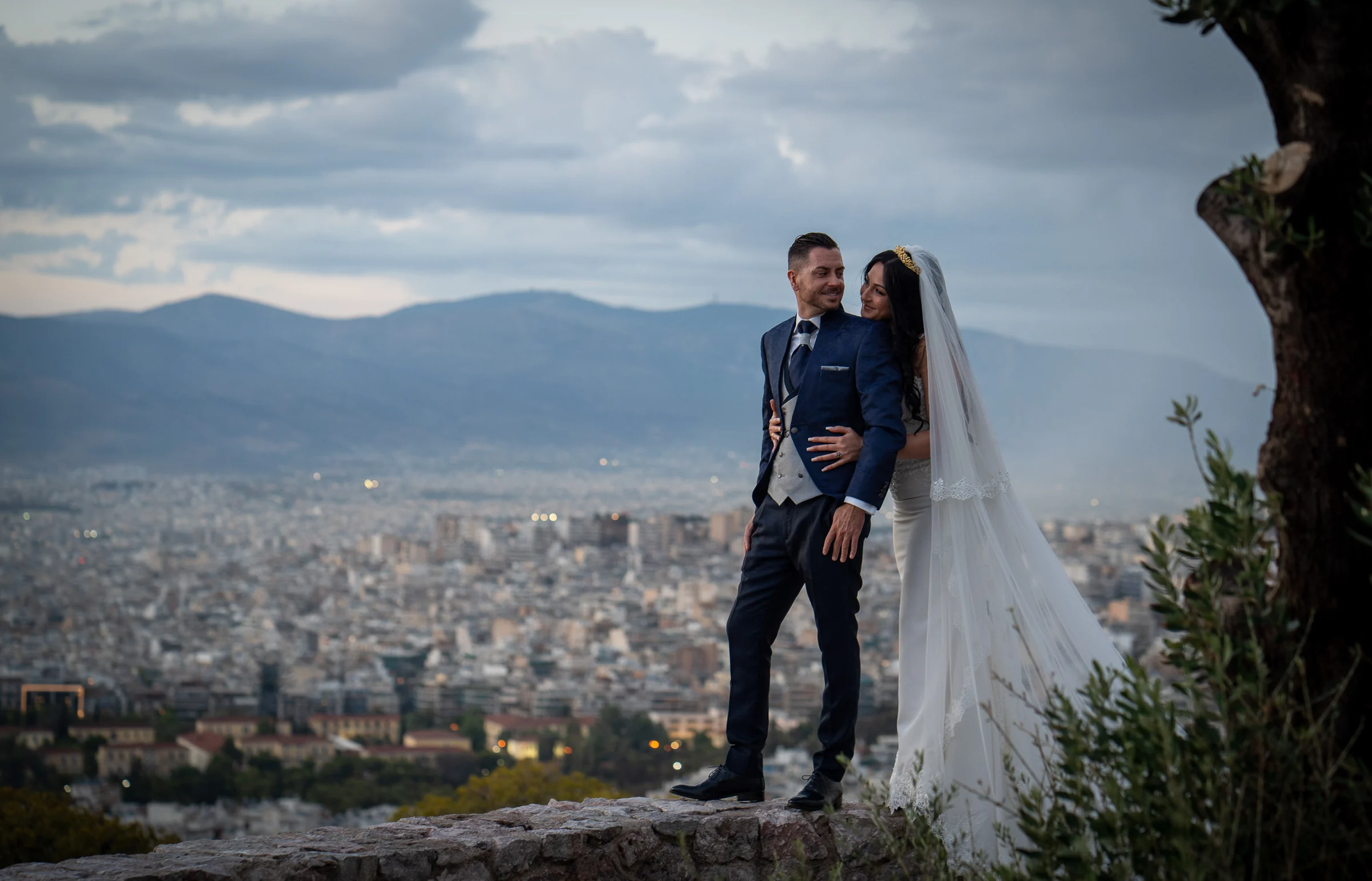 Sara y Edu comparten una mirada con una amplia panorámica de Atenas y sus montañas al fondo durante su postboda.