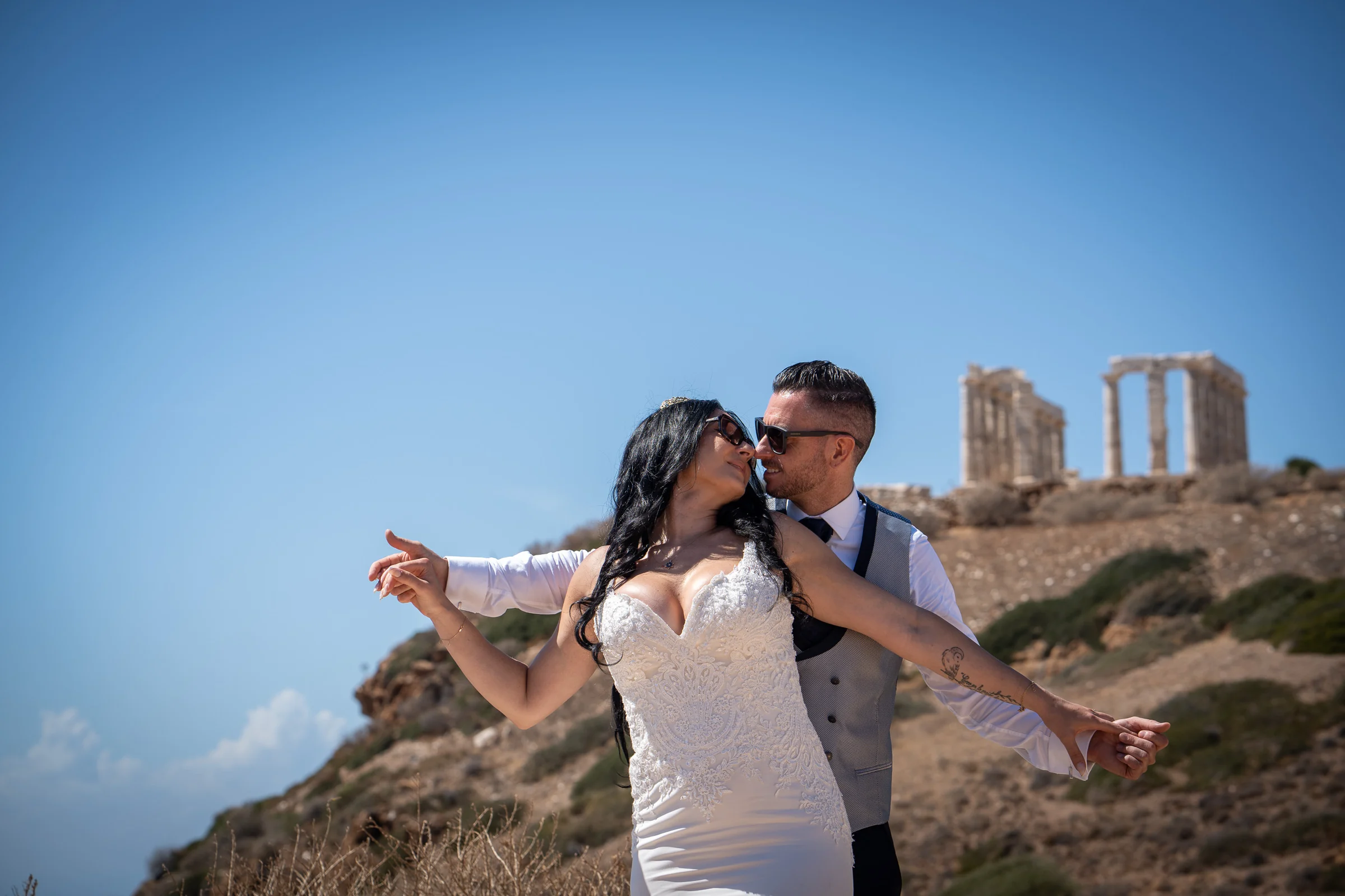 Sara y Edu se abrazan ante unas ruinas clásicas junto a la costa griega durante su postboda en Grecia.