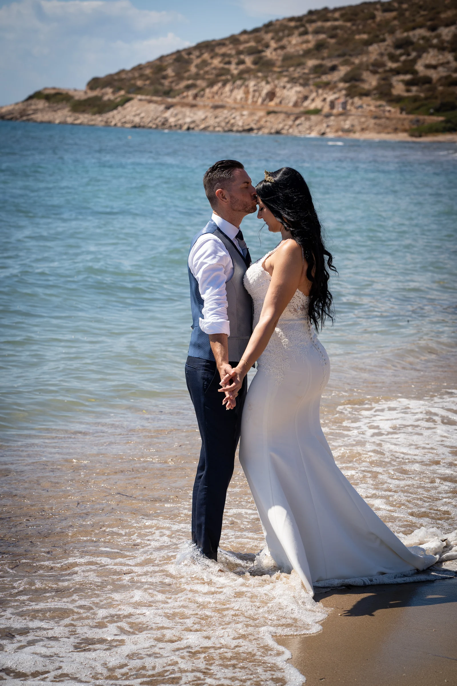 Edu besa la frente de Sara mientras permanecen de la mano dentro de la orilla del mar durante su postboda en Grecia.