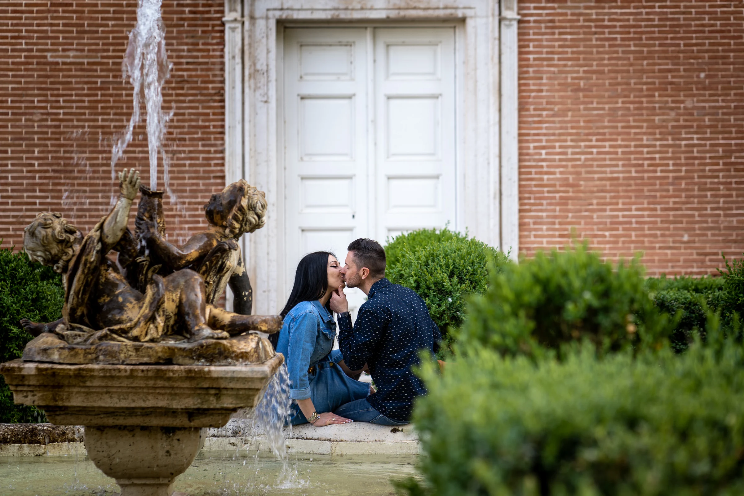 Sara y Edu se besan junto a una fuente ornamental durante su preboda en el entorno del Palacio Real de Aranjuez.