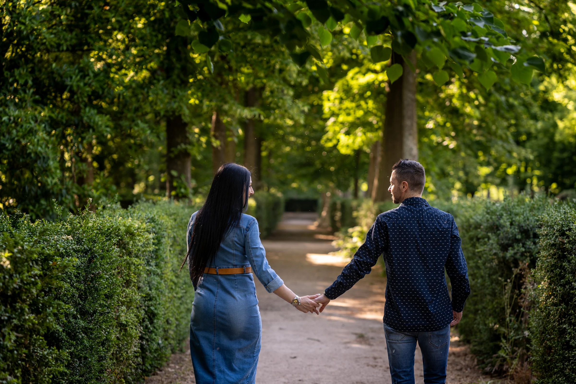 Sara y Edu caminan de la mano entre setos y árboles durante su preboda en los jardines de Aranjuez.