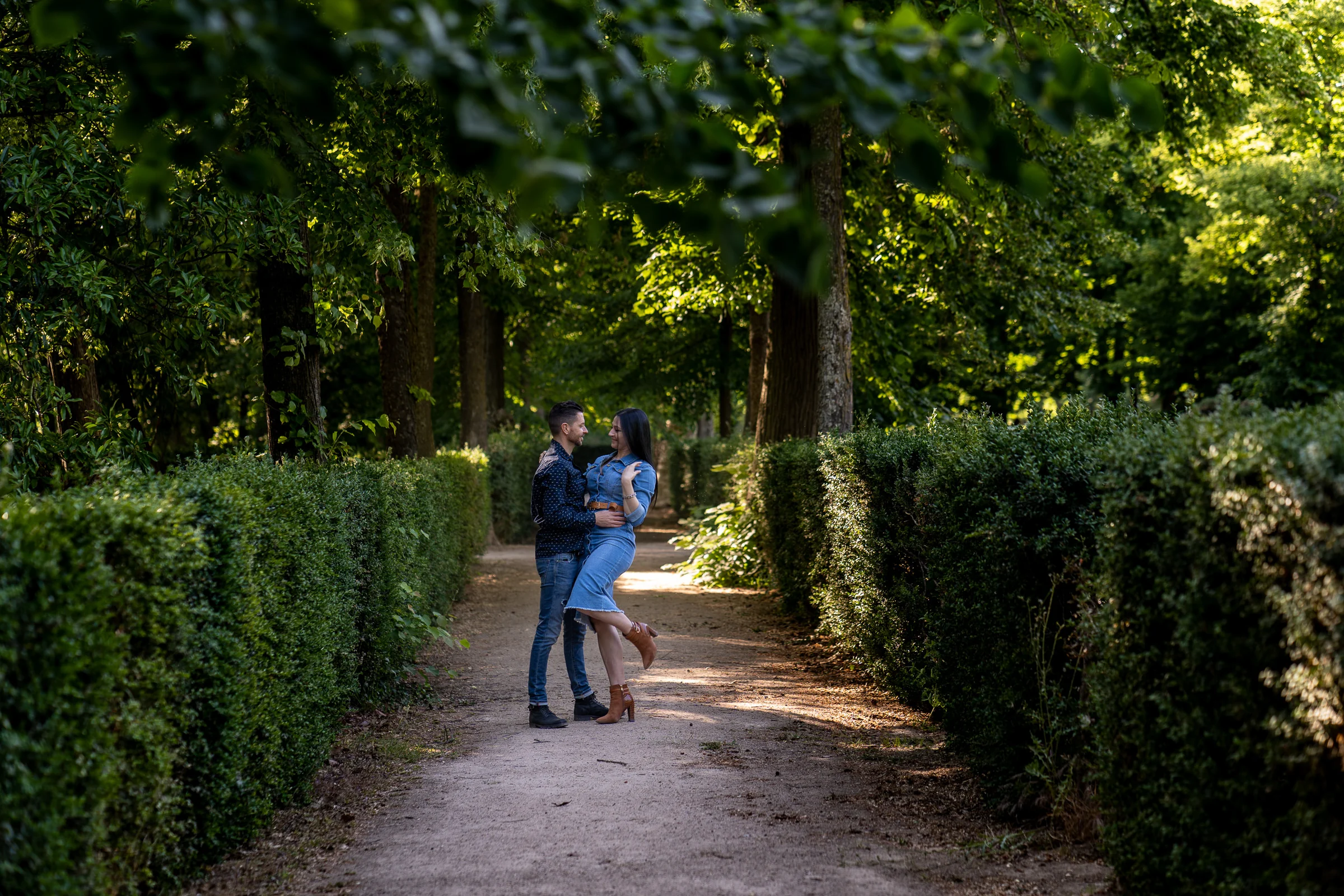 Sara y Edu juegan y se abrazan en un sendero entre setos durante su preboda en los jardines de Aranjuez.