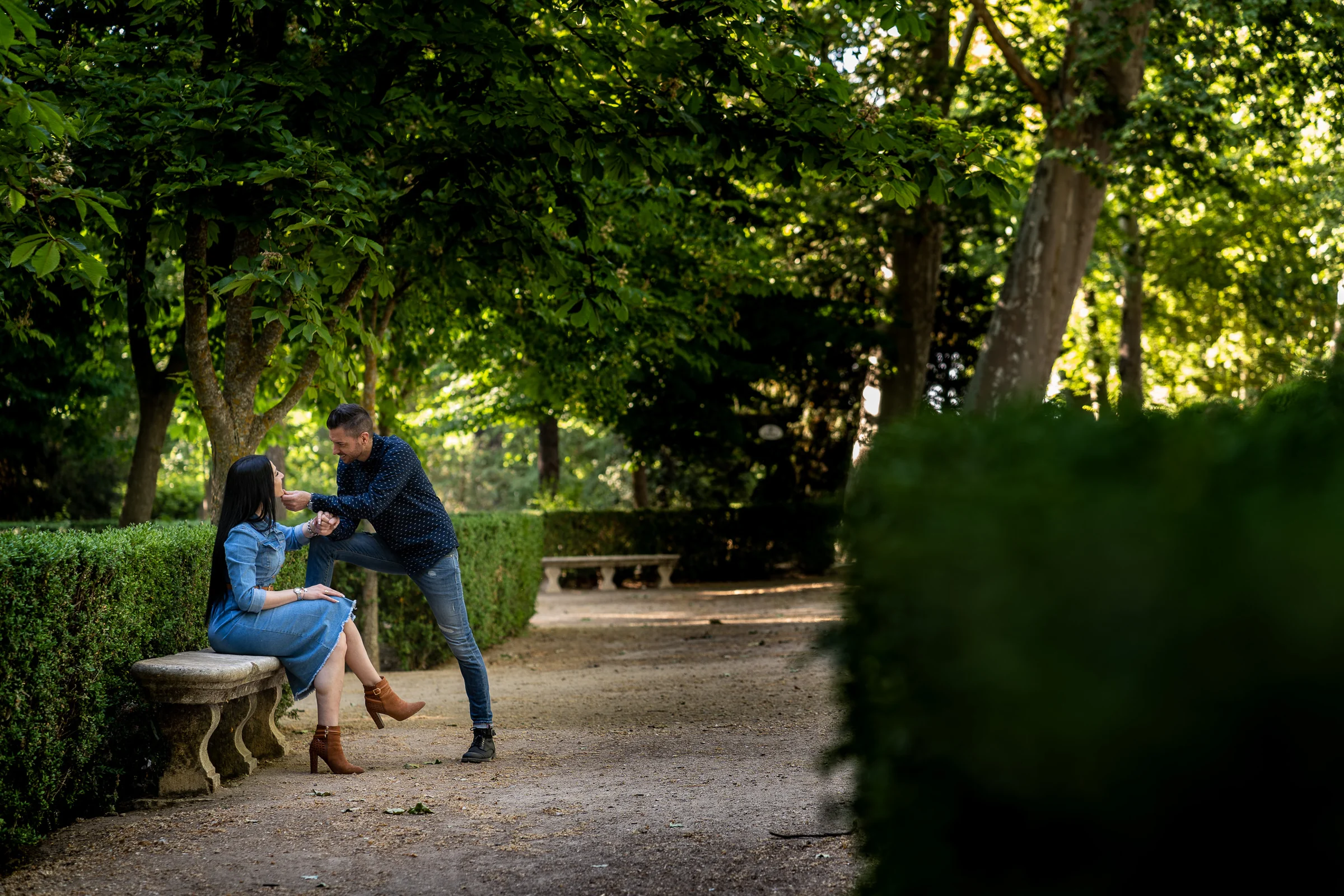 Sara y Edu comparten un momento junto a un banco de piedra en los jardines de Aranjuez durante su preboda.