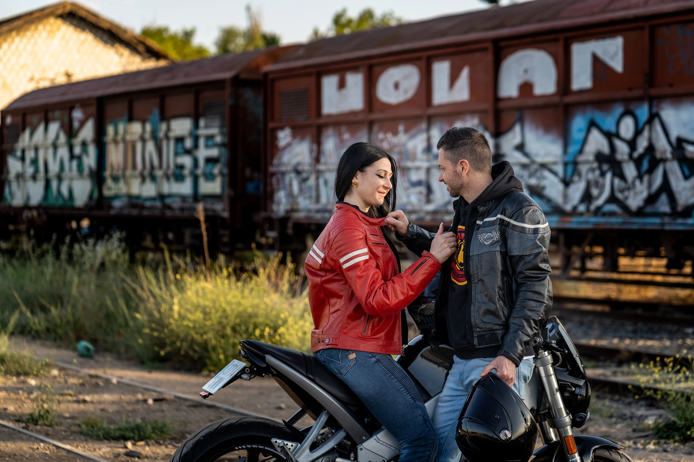 Sara y Edu comparten una mirada junto a su moto en un entorno ferroviario de Aranjuez durante su preboda.