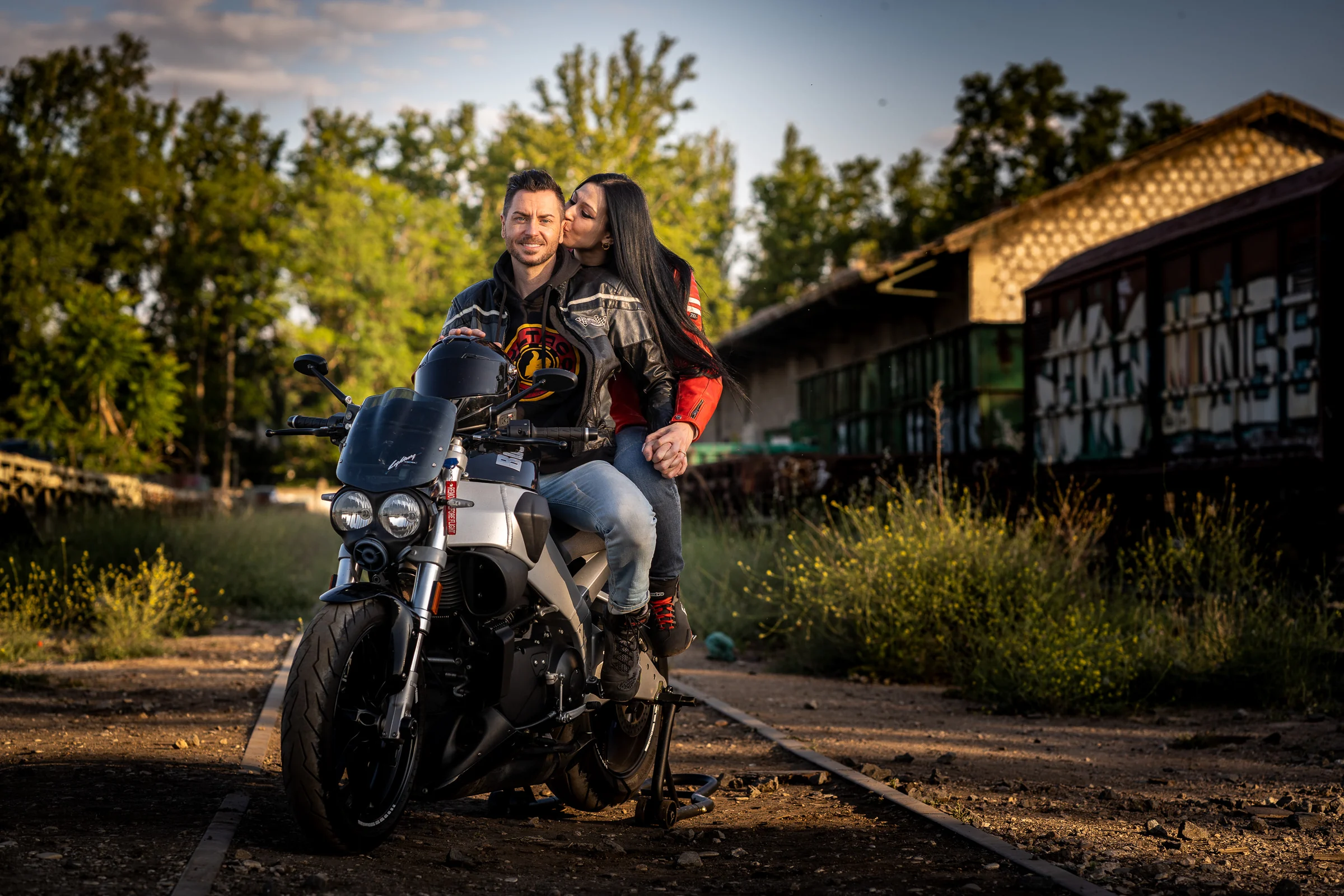 Sara y Edu posan sobre una moto entre vías y antiguas estructuras ferroviarias durante su preboda en Aranjuez.