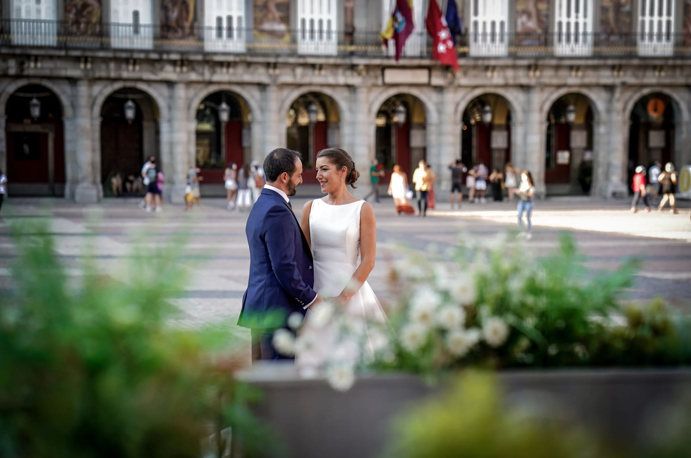 Sara y Edu comparten una mirada en la Plaza Mayor fotografiados entre flores y terrazas durante su postboda en Madrid.
