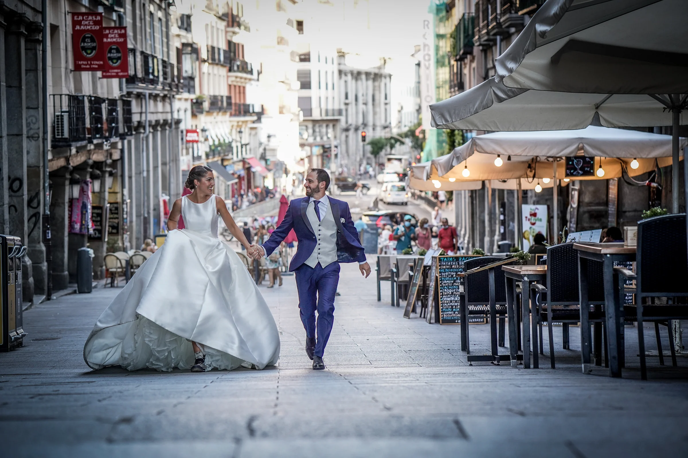 Sara y Edu caminan de la mano por una calle del Madrid de los Austrias durante su sesión de postboda en el centro de Madrid.