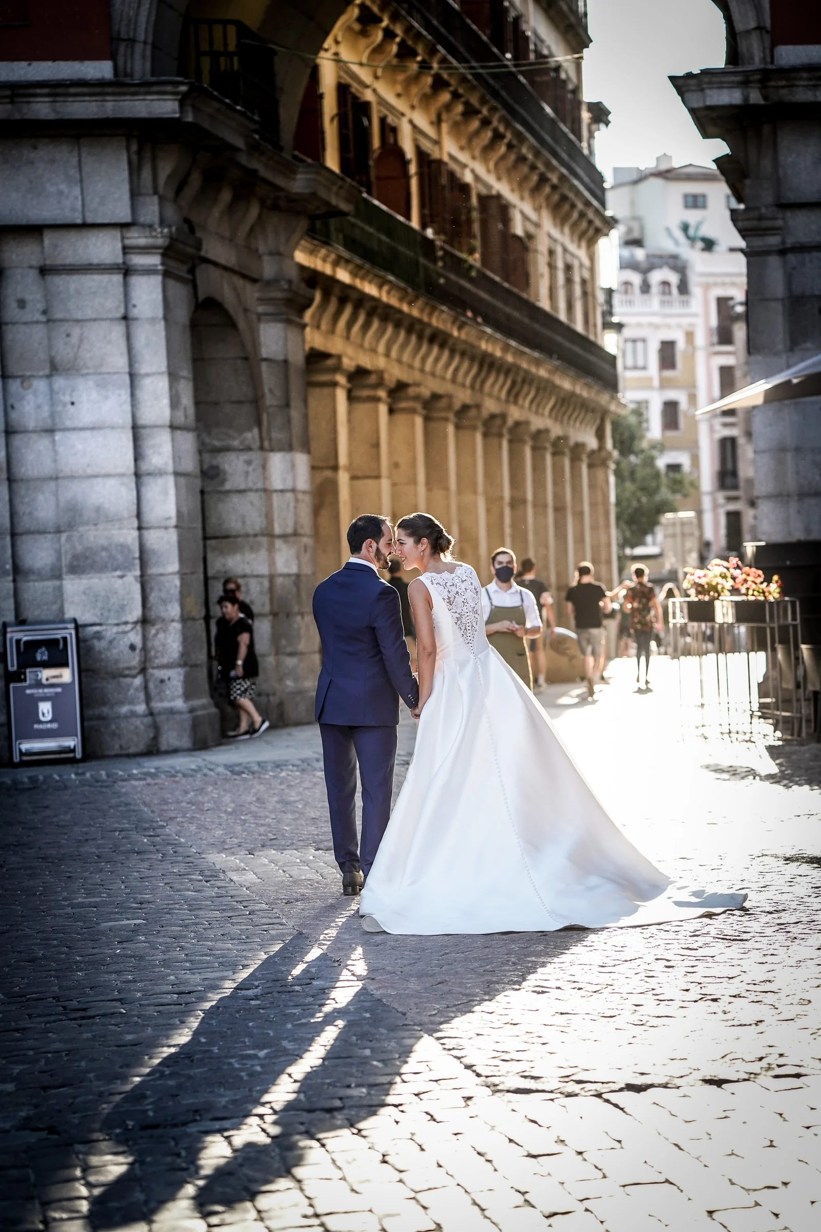 Sara y Edu caminan juntos por una calle adoquinada del Madrid de los Austrias iluminada por el sol de la tarde.