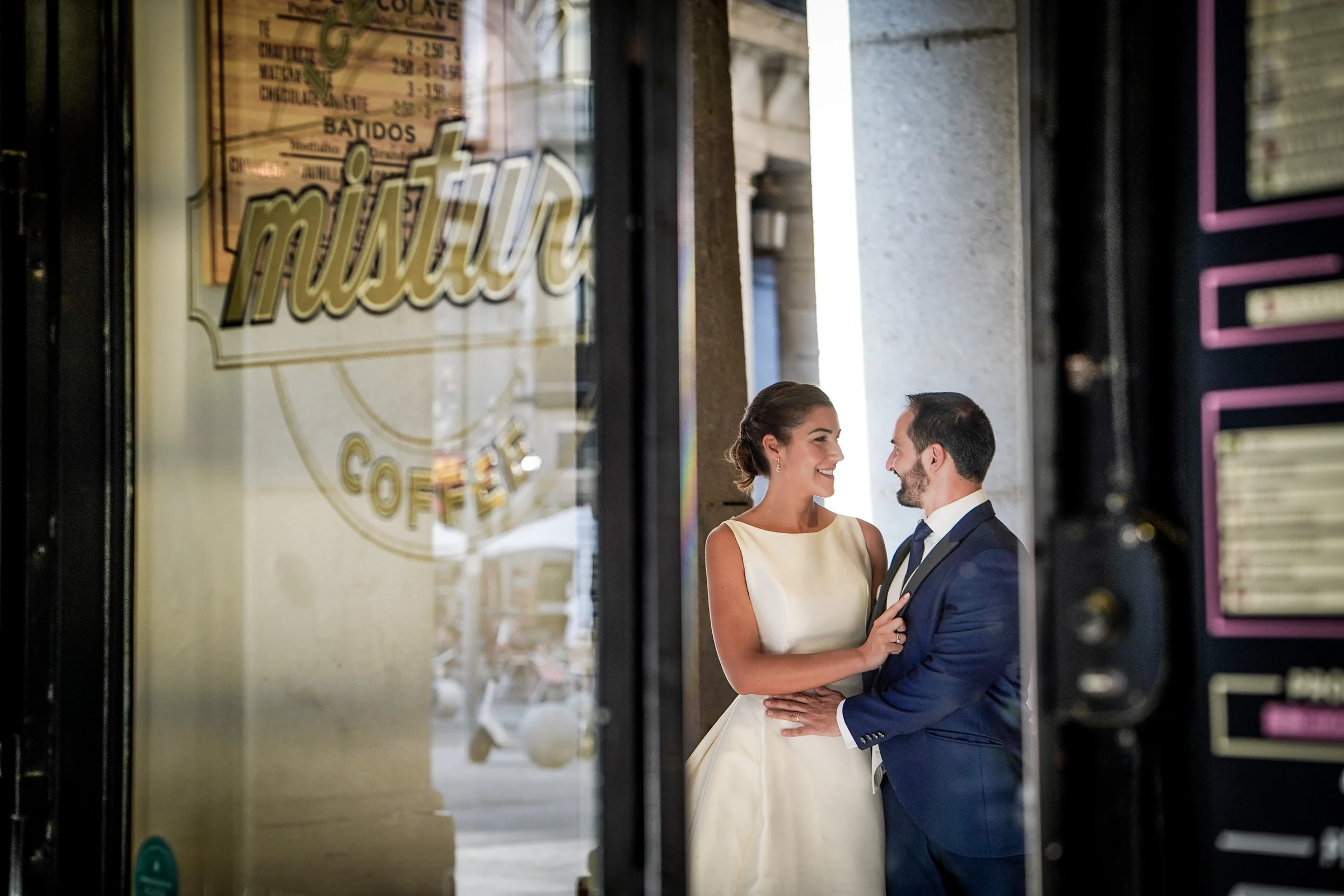 Sara y Edu se miran junto al escaparate de una cafetería del centro de Madrid durante su postboda por la zona de la Plaza Mayor.