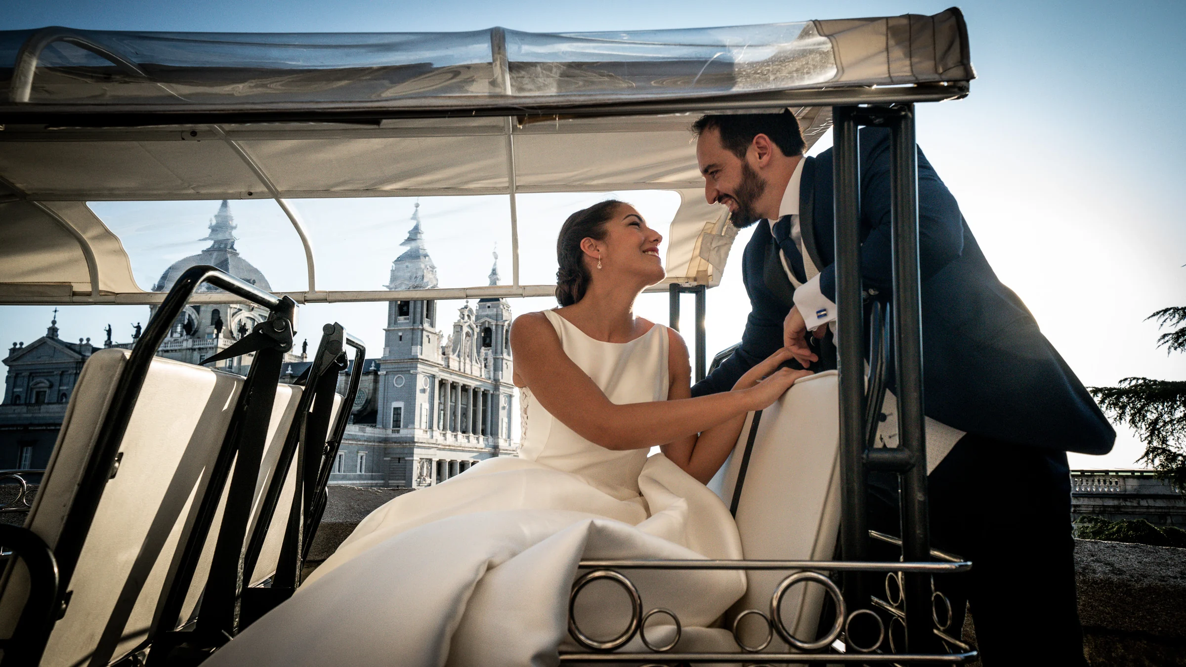 Sara y Edu comparten un momento en un vehículo urbano con la Catedral de la Almudena al fondo durante su postboda en Madrid.